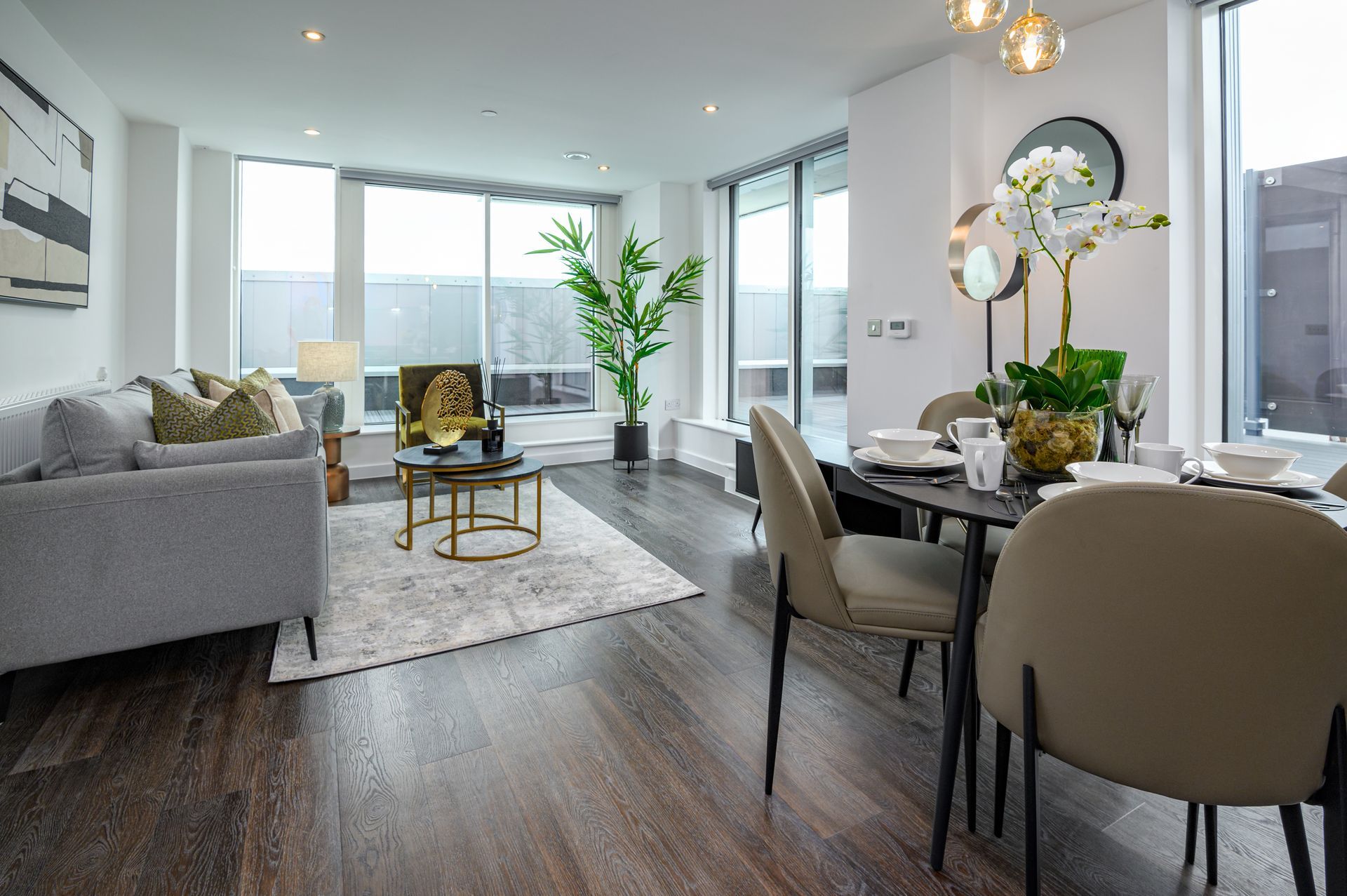 Bright modern living and dining room with gray sofa, dining table, and floor-to-ceiling windows