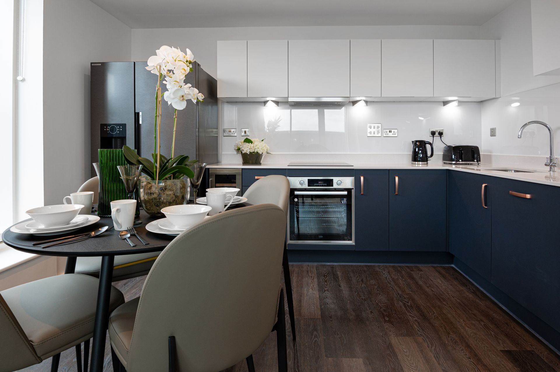 Modern kitchen with navy cabinets, white countertops, and a dining table set for two.