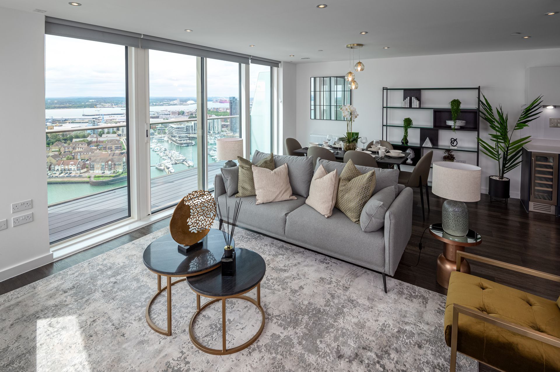 Bright living room with floor-to-ceiling windows, gray sofa, coffee tables, and city view