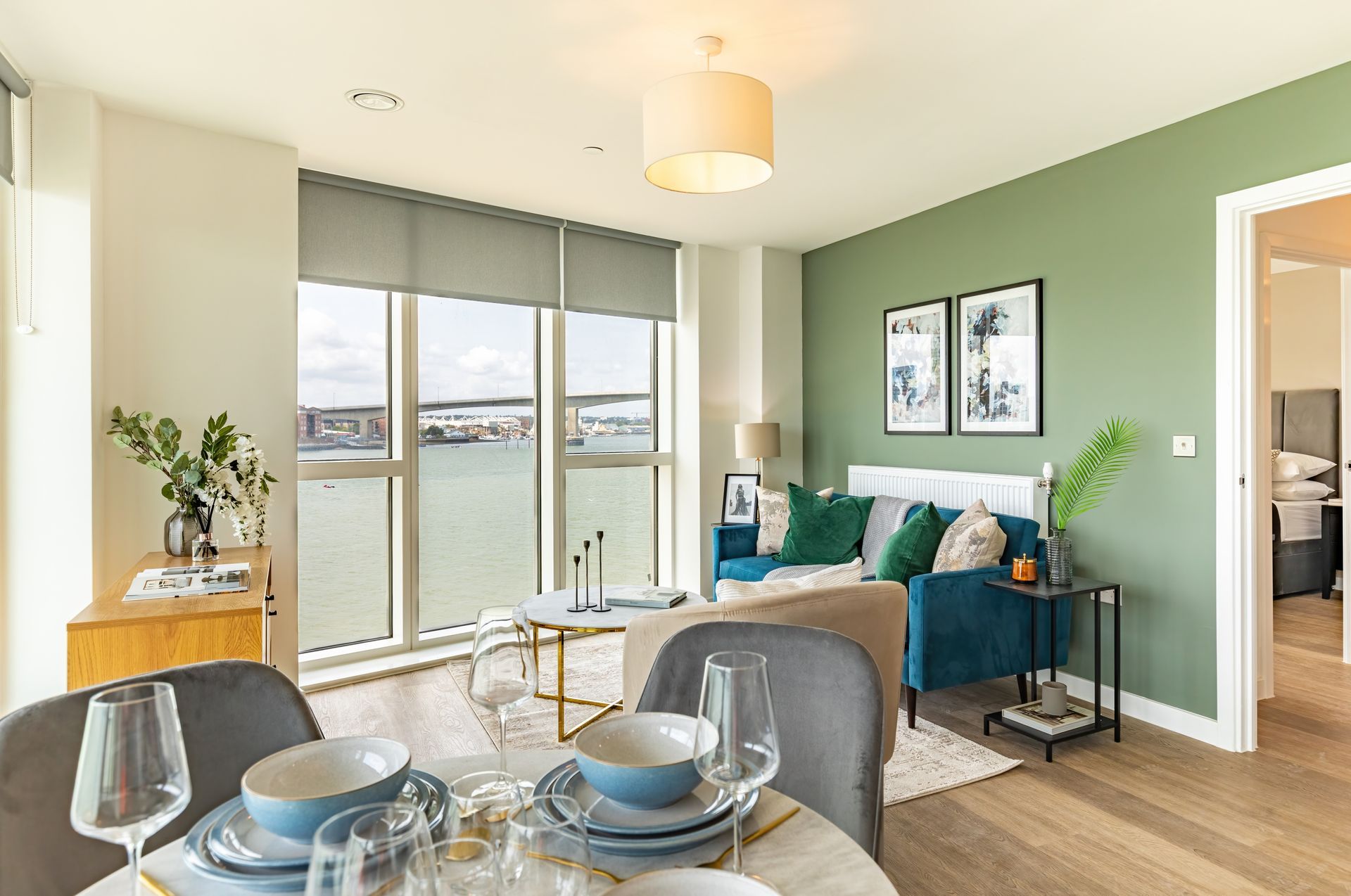 Bright living room with green accent wall, sofa, dining table, and large windows overlooking water