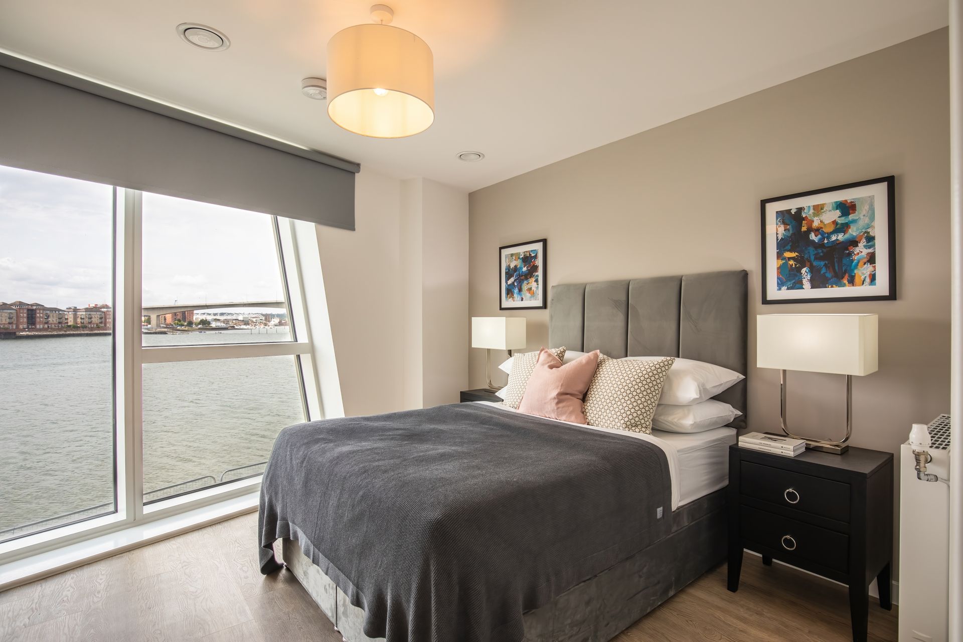 Modern bedroom with gray bed, nightstands, and large window overlooking the water