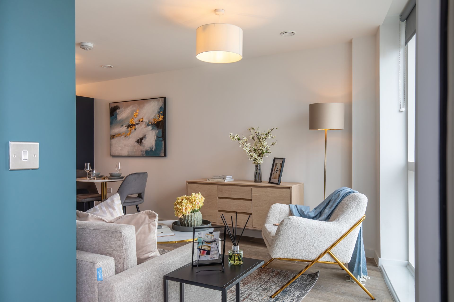 Modern living room with beige and white furniture, abstract wall art, and large windows.