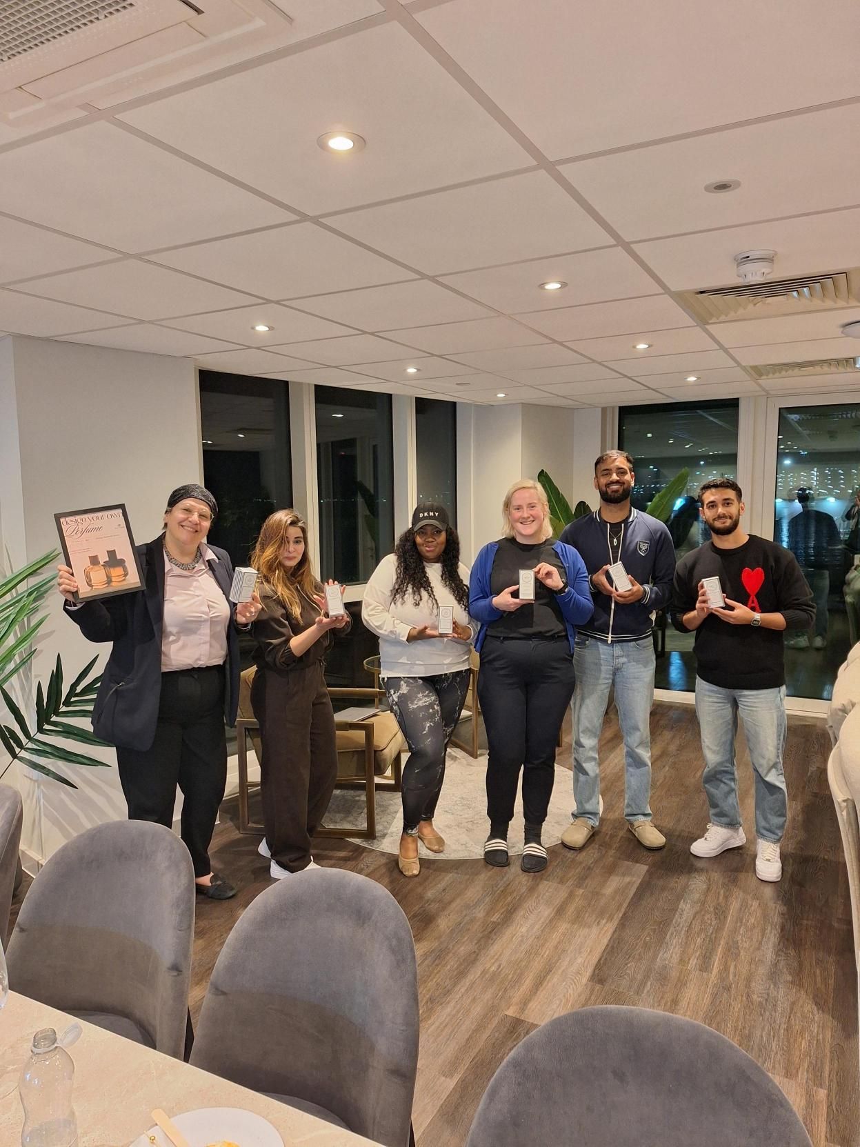 Group of people standing indoors in an office, smiling and holding small awards at a celebration.