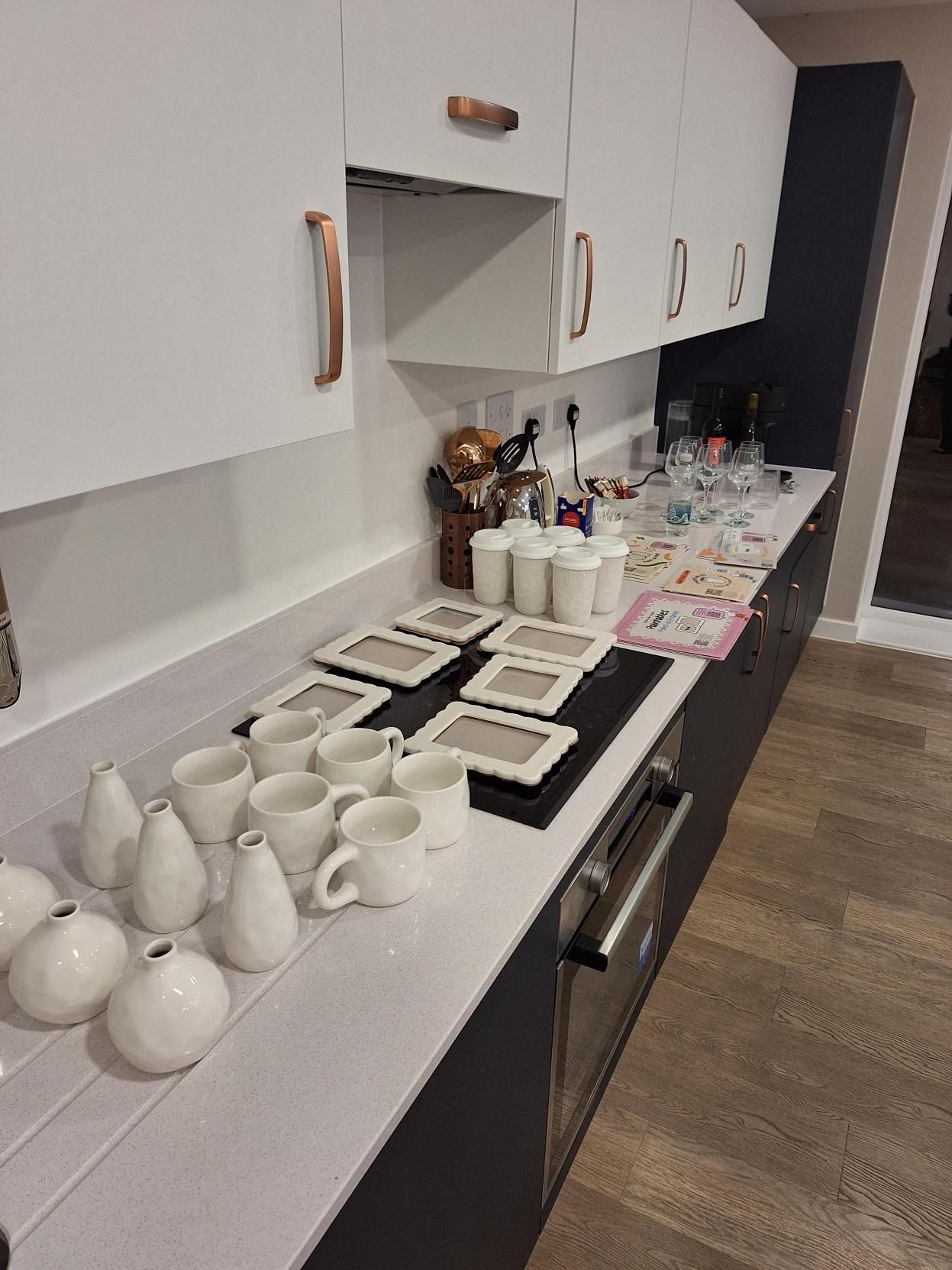 Kitchen counter lined with white cups, mugs, and saucers beside an open cabinet and sink area