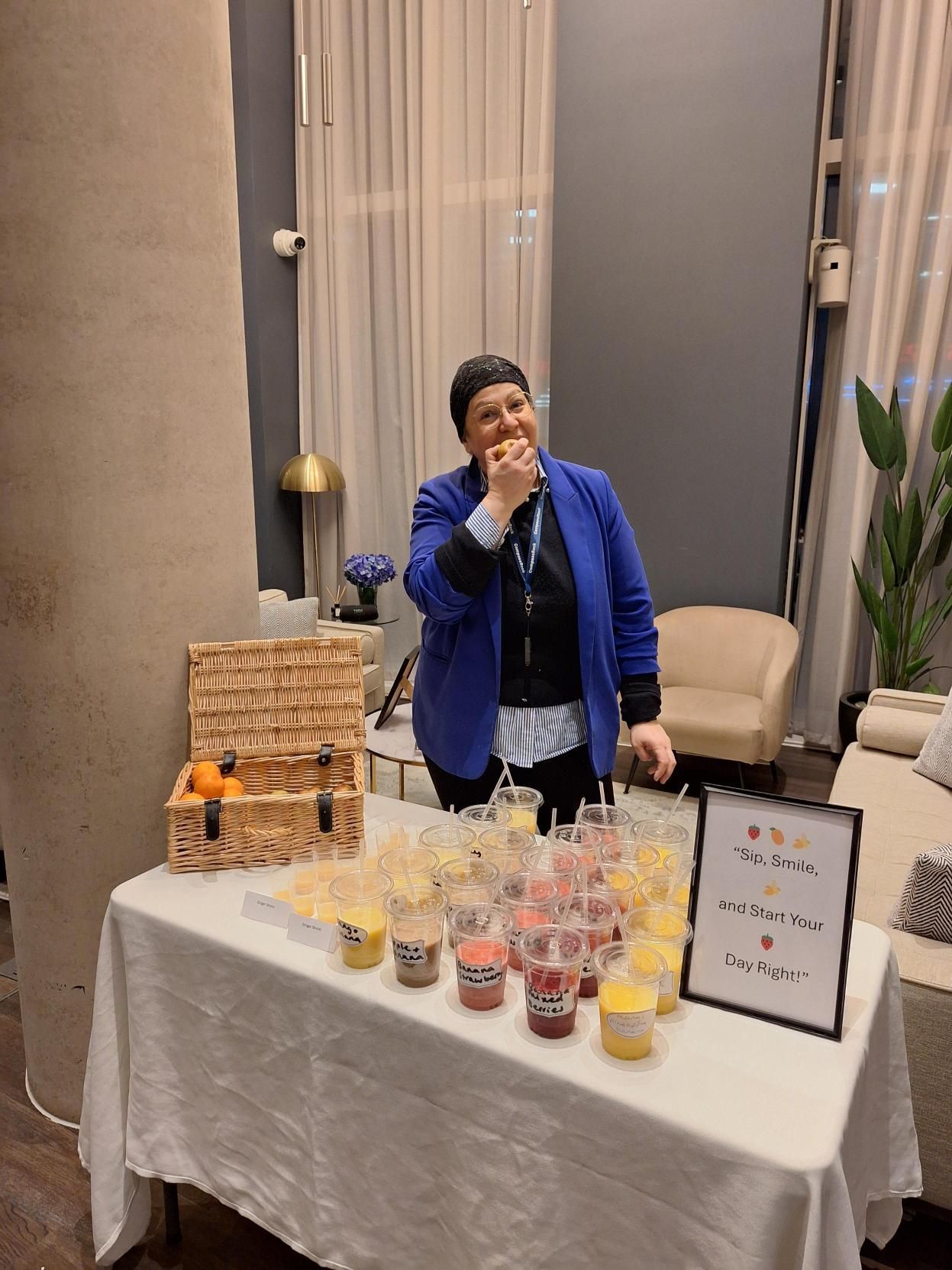 Woman sampling drinks at a vendor table with cups and a sign in a hotel lobby
