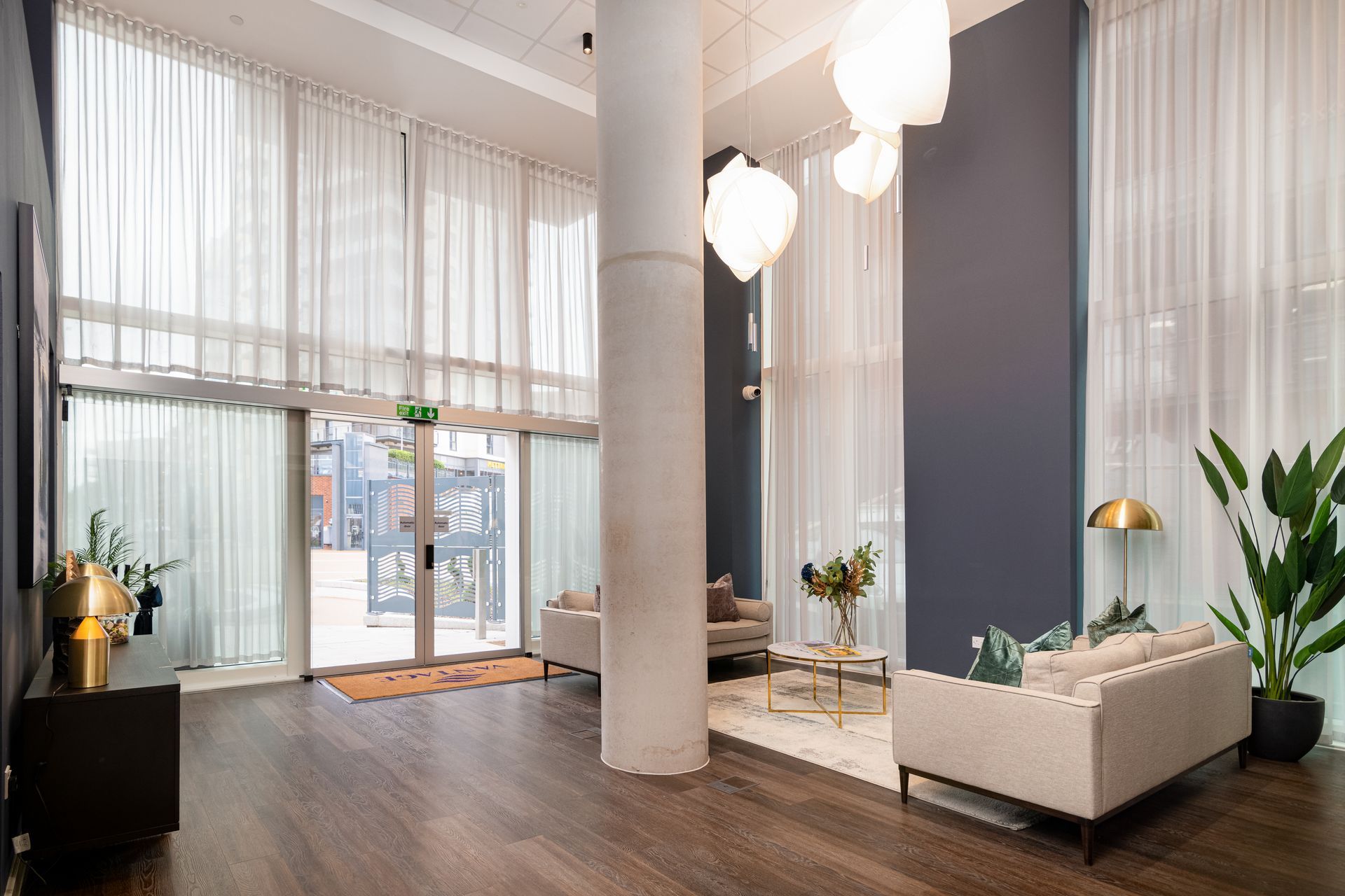 Bright modern lobby with tall windows, white columns, wood floors, and white seating areas