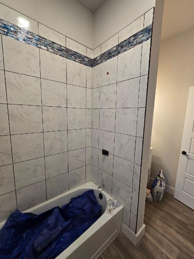 Partially tiled bathroom shower under renovation, with a blue tarp covering the tub and tiled walls unfinished.