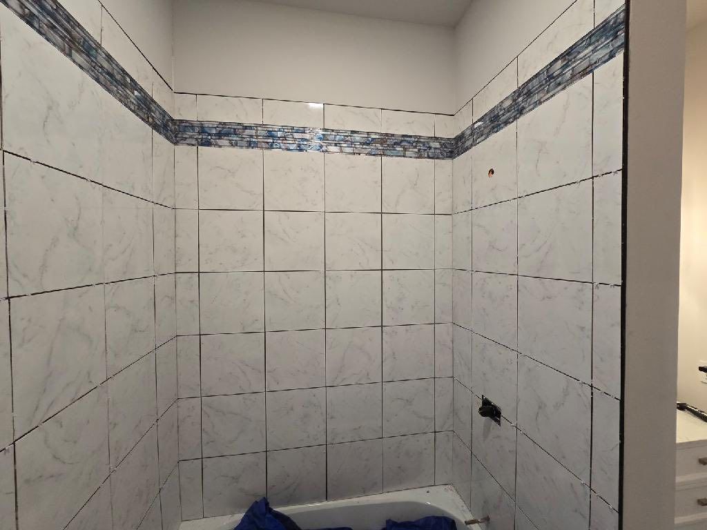 Small tiled bathroom shower alcove with white walls, blue border tile, and a built-in tub below.