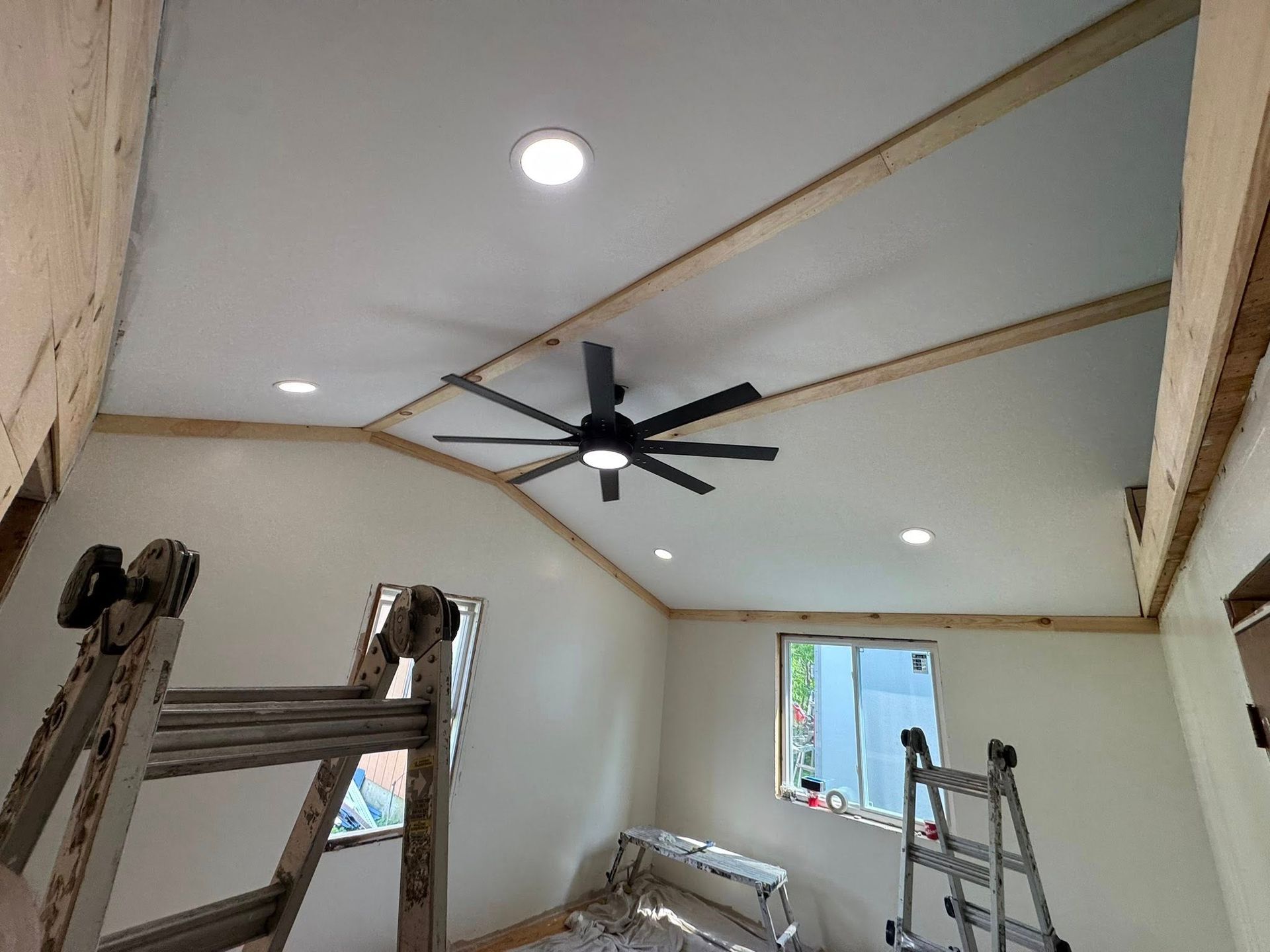 Interior room with vaulted ceiling, black ceiling fan, recessed lights, ladders, and a window
