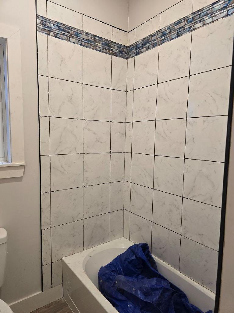 Small tiled bathroom shower-tub corner with a blue plastic bag draped over the tub edge.