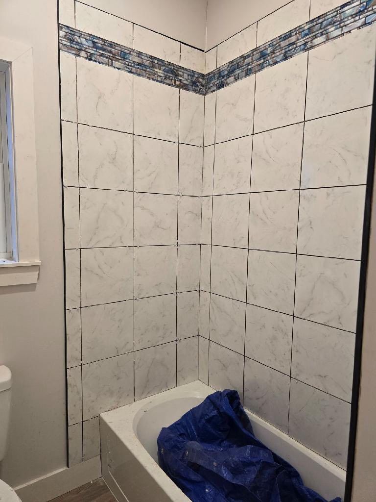 Bathroom shower/tub corner with white tiled walls and blue decorative border, blue cloth in the tub