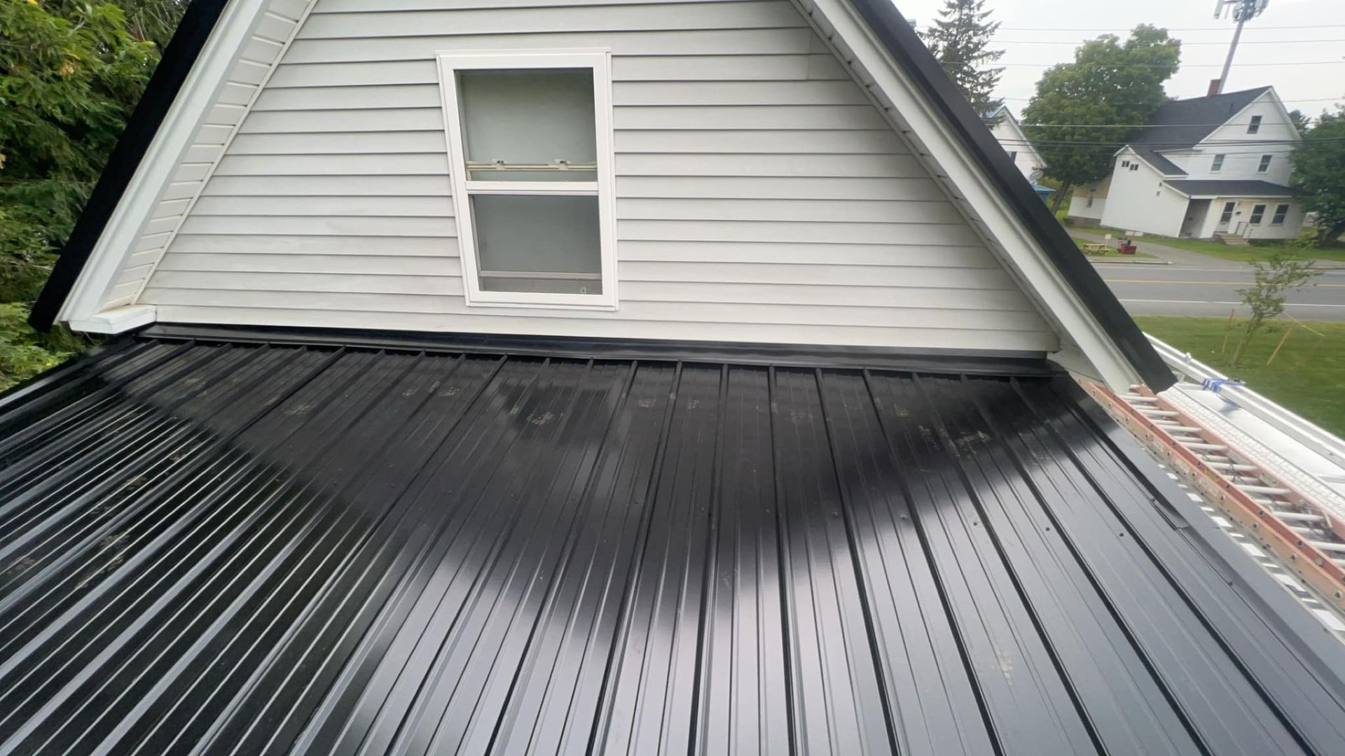 Black standing-seam roof with a white dormer window on a house, viewed from above.