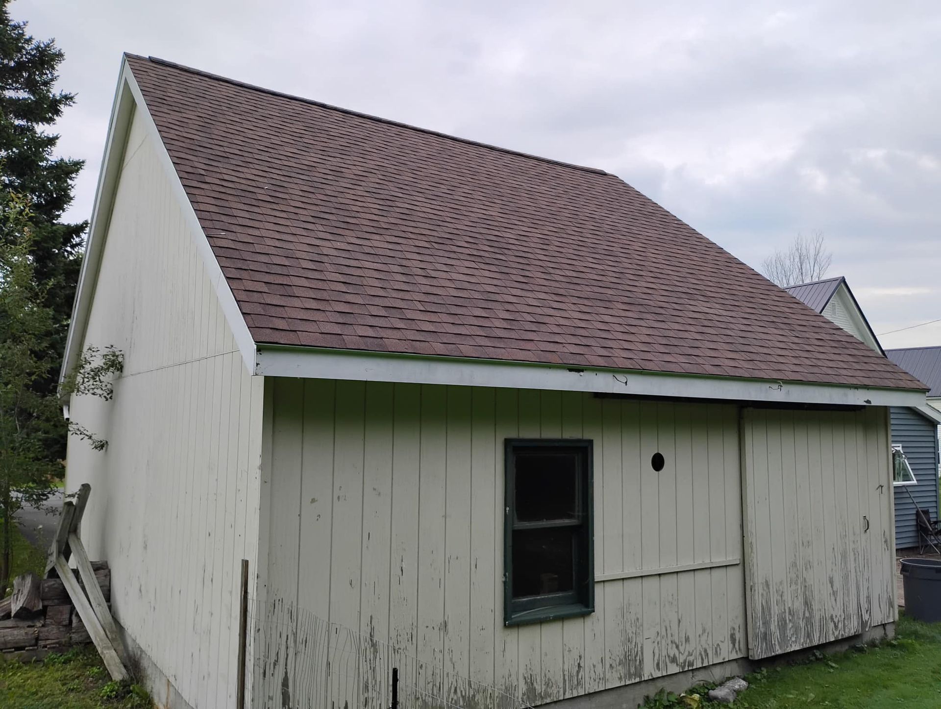 Small white shed with a red shingled roof and dark door window, seen from the side outdoors.