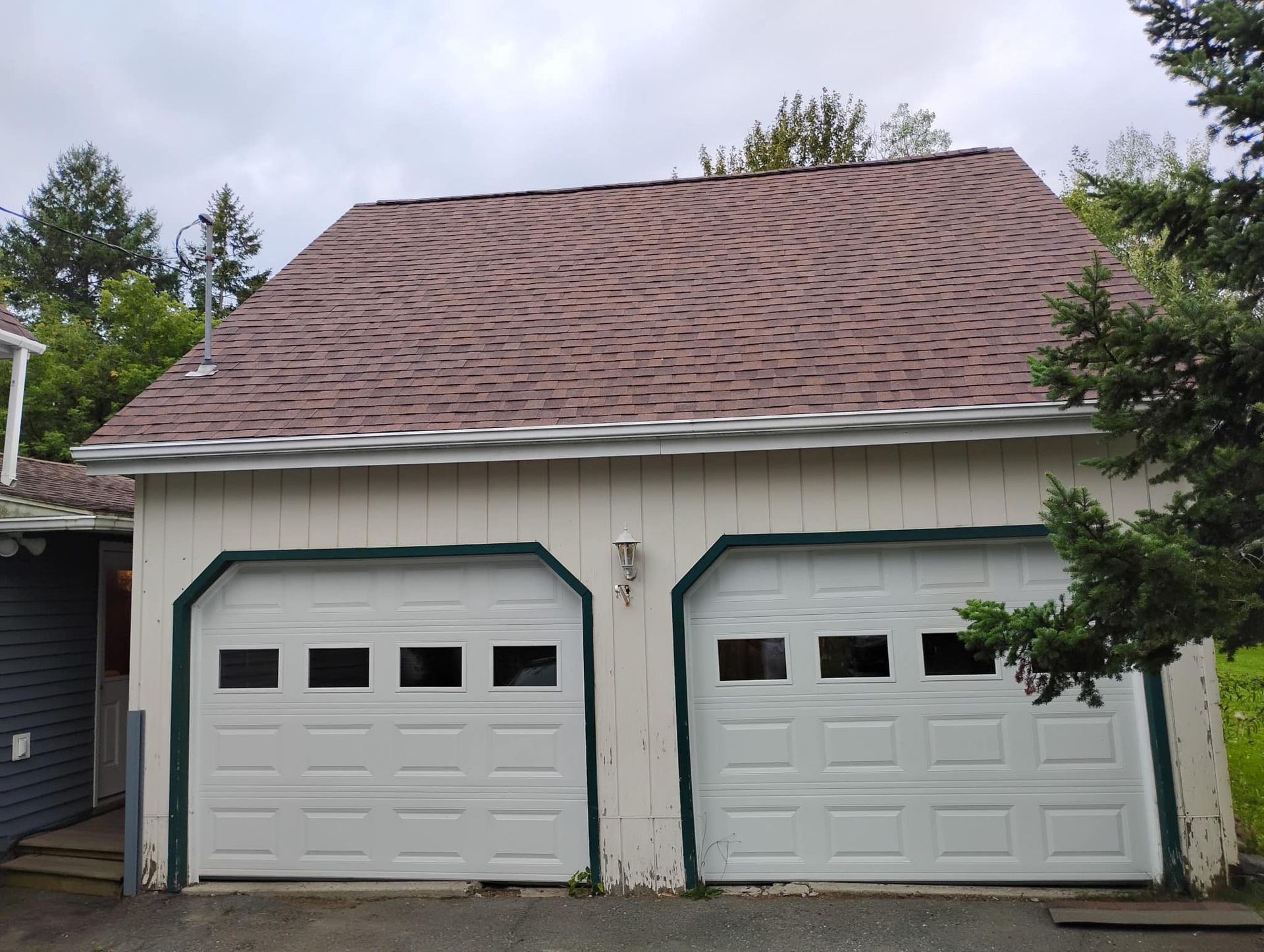 Two-car garage with green-trimmed white doors and a wavy brown shingle roof