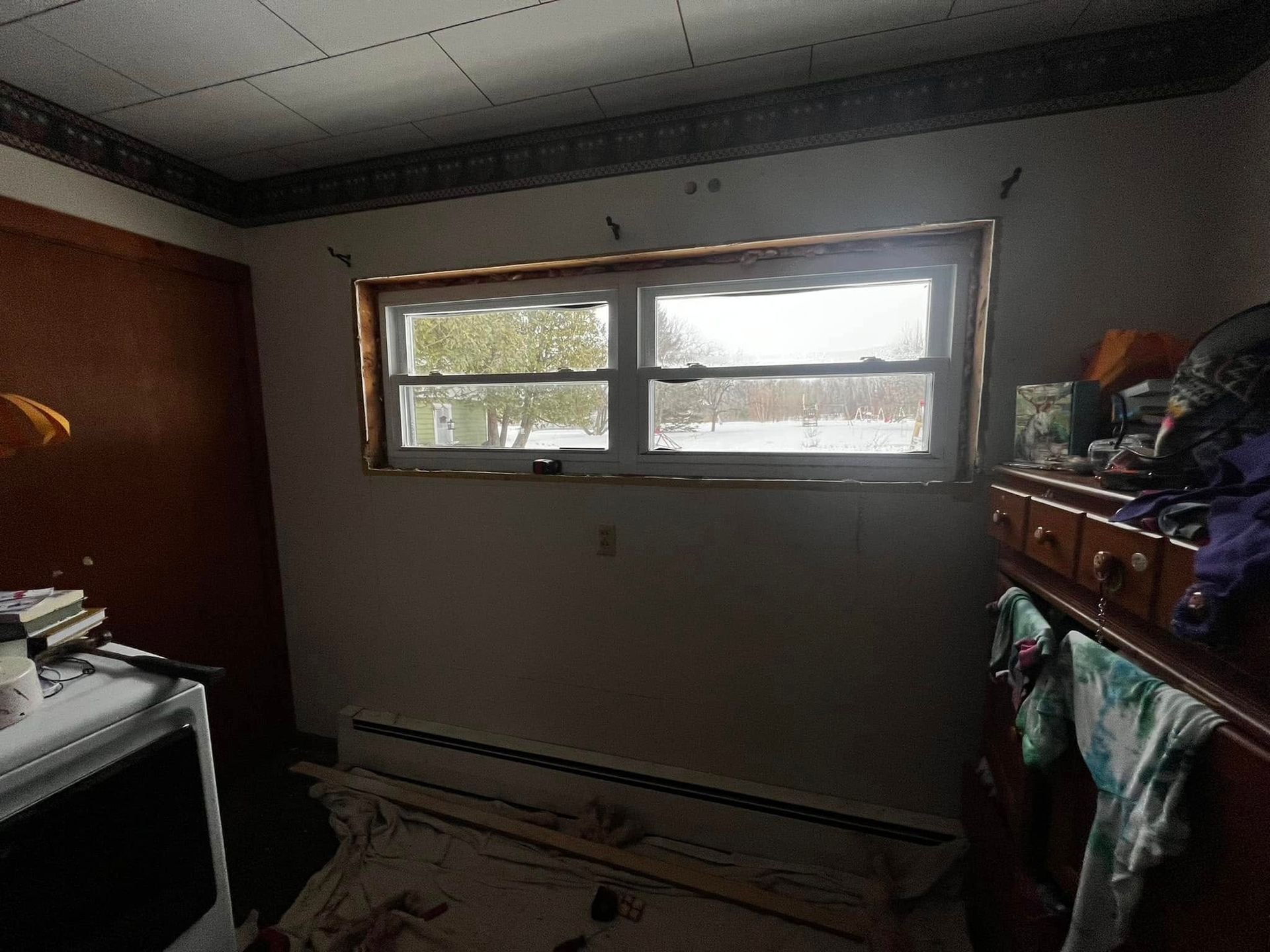 Small cluttered bedroom with a window, wooden dresser, and a TV on the left.