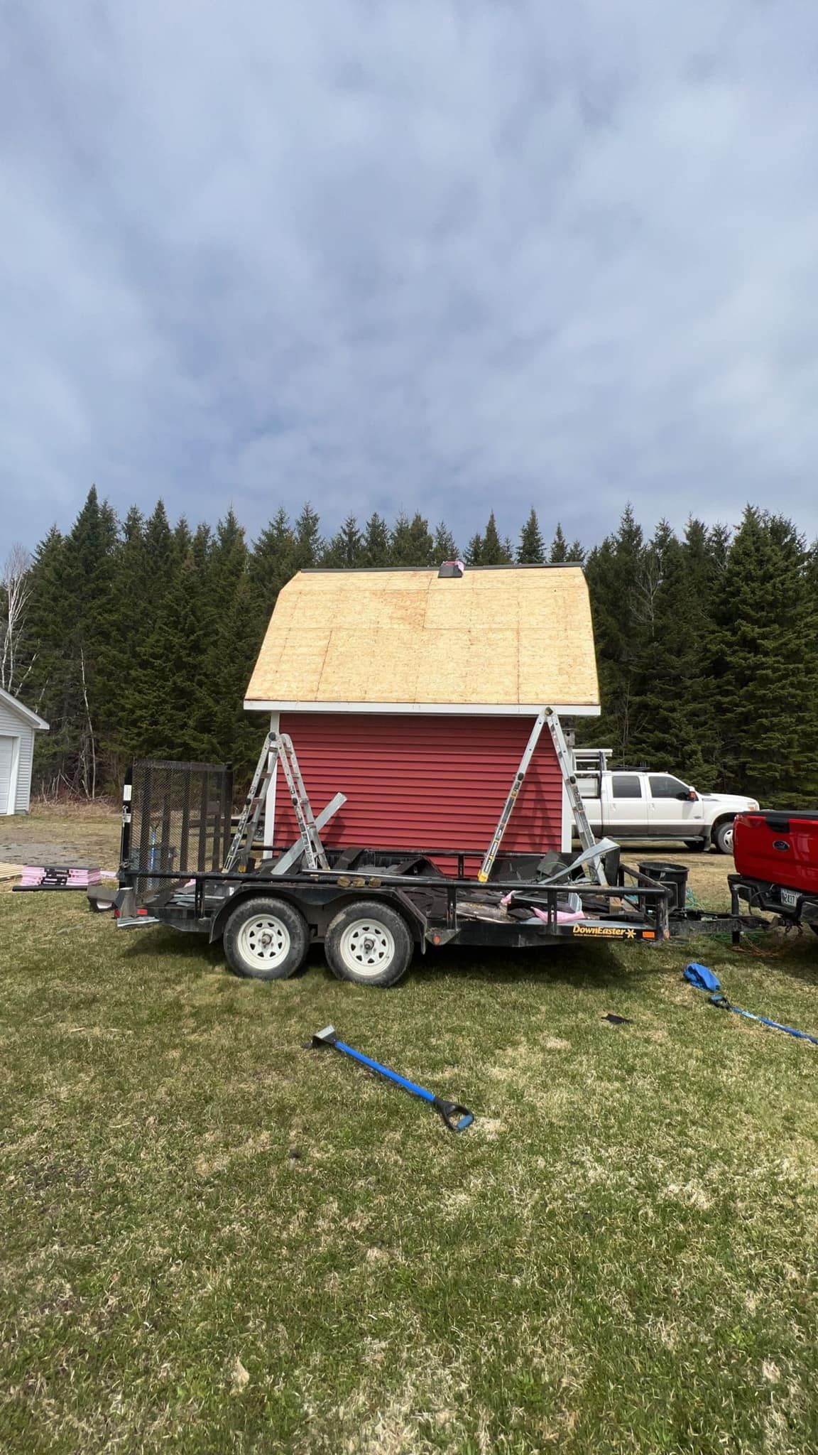 Small red shed on a trailer in a grassy yard with a white truck and trees in the background