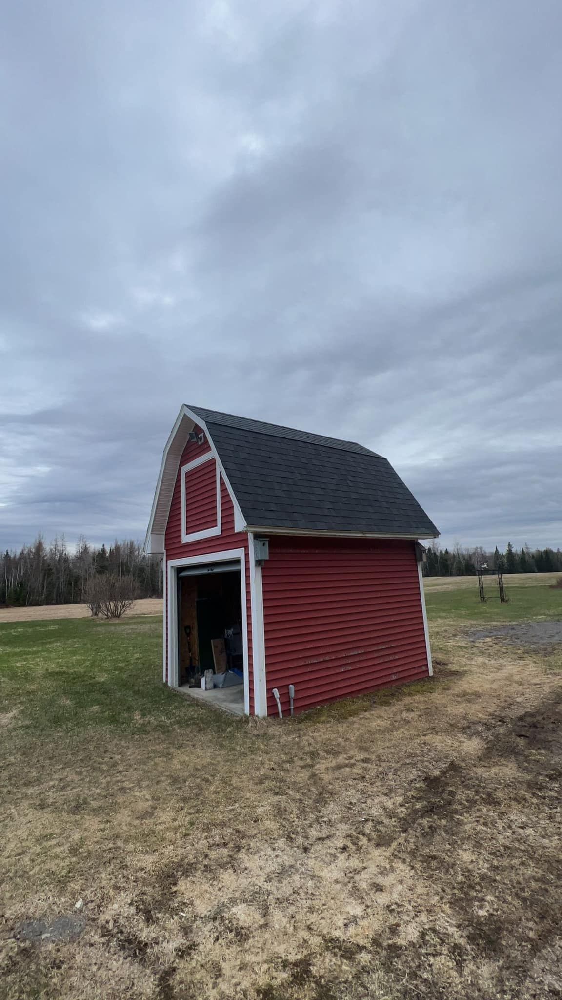 Small red barn-like shed with white trim on a grassy field under a cloudy sky