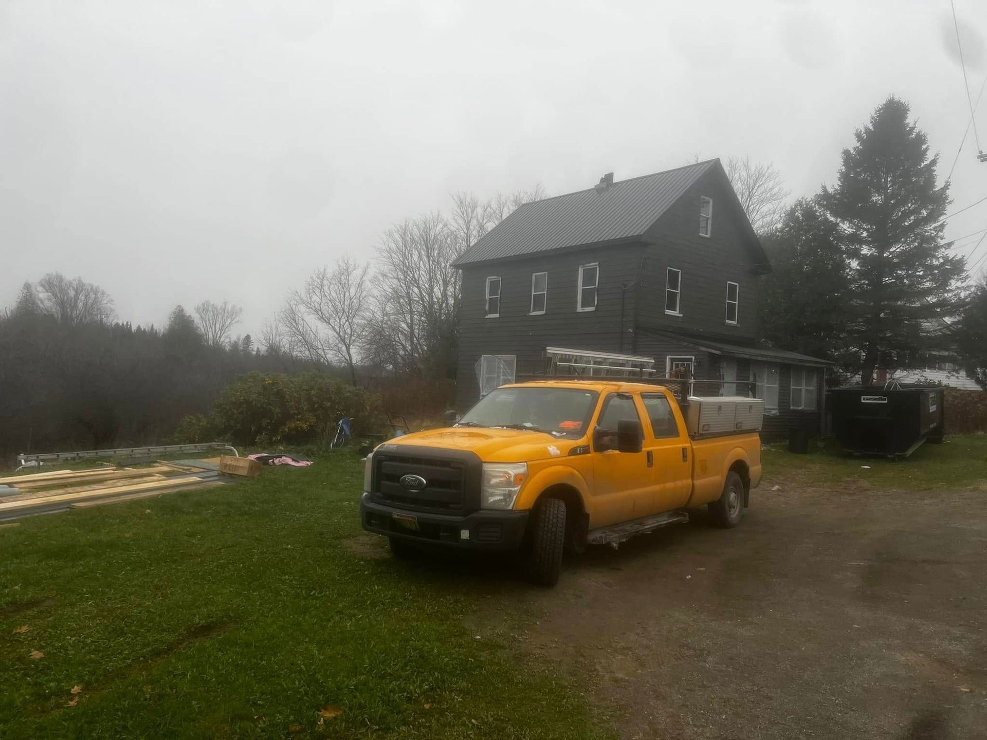 Yellow pickup truck parked in front of a dark two-story house on a cloudy rural property