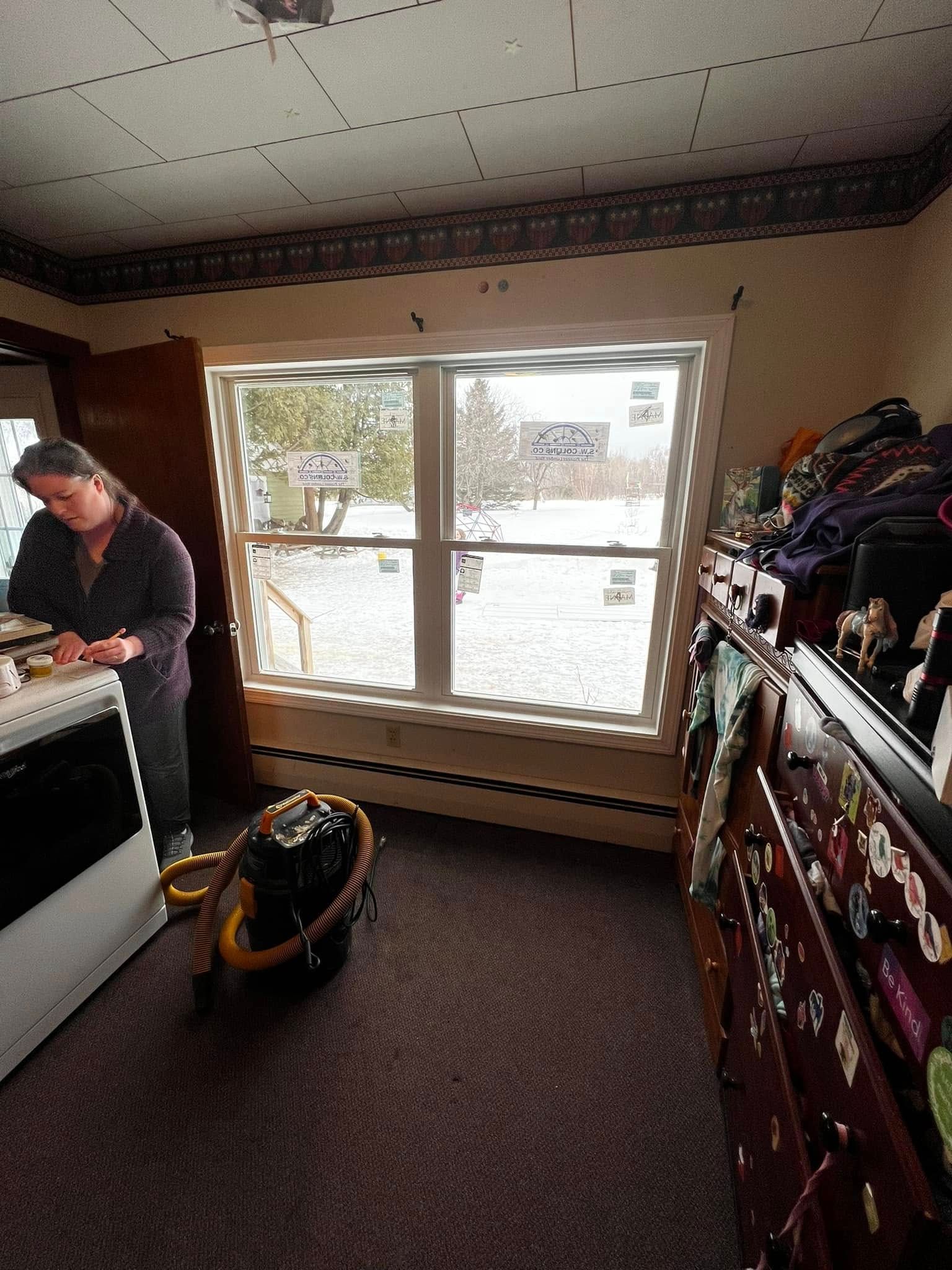 Small living room with a large window, a person at left, and a vacuum cleaner on the floor