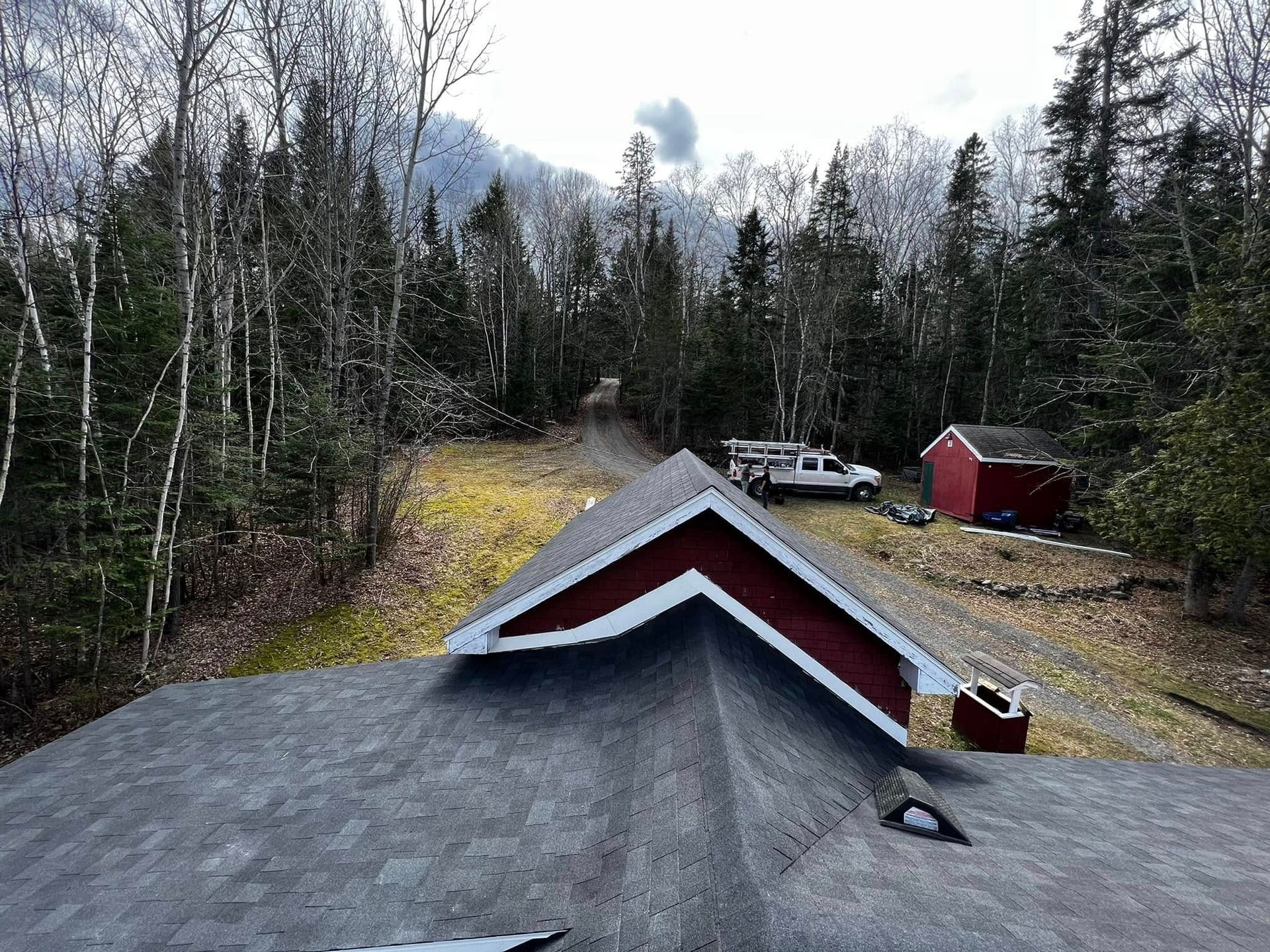 Rooftop view of a gravel driveway, red shed, parked pickup, and leafless trees in a wooded rural area