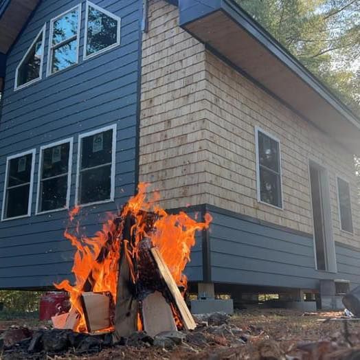 Bonfire burning beside a blue-and-beige house under construction