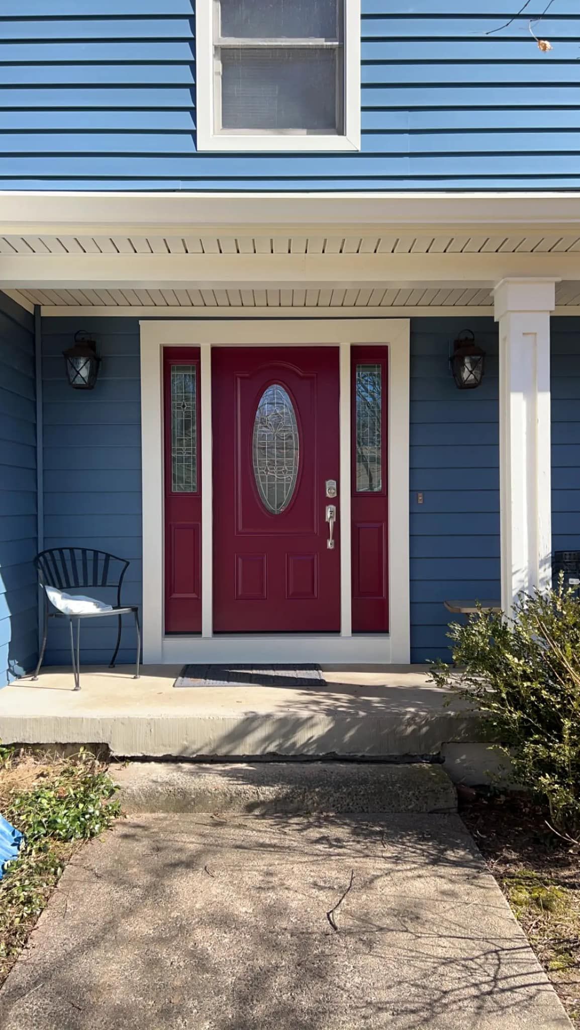Blue house front entrance with red double doors, white trim, and a chair on the porch