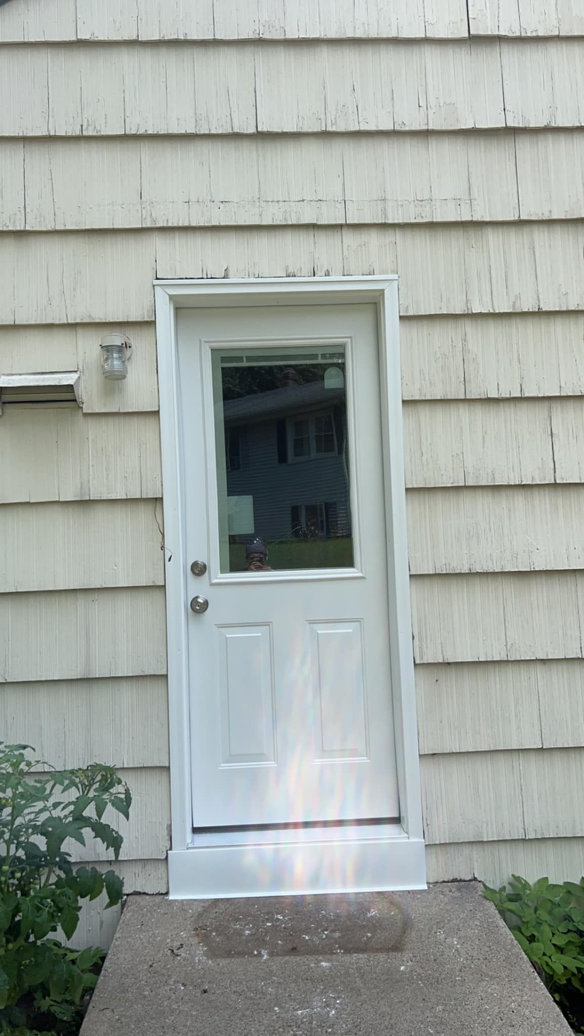 White exterior door with window in beige shingled wall, centered above a small concrete step.