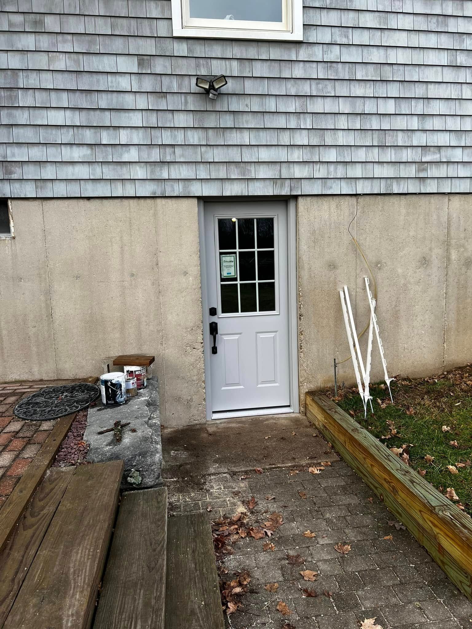 Back door entrance with white door, concrete path, and weathered shingle siding.