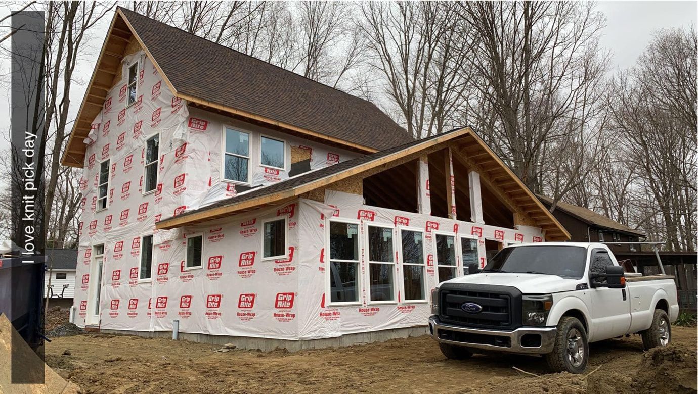 Partially built house wrapped in Tyvek, with a white pickup truck parked in front