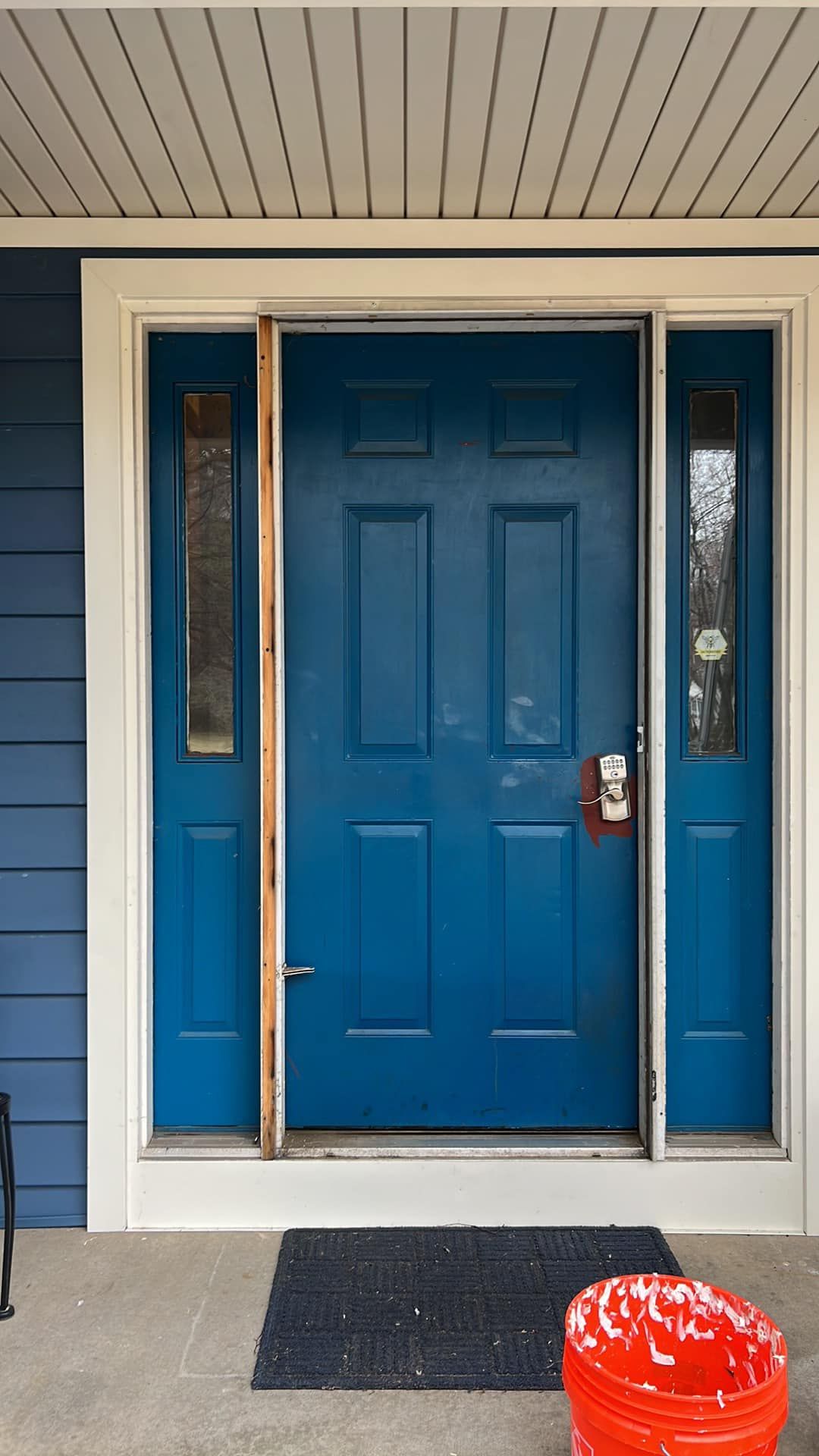 Blue front door with sidelights and a red bucket on the porch