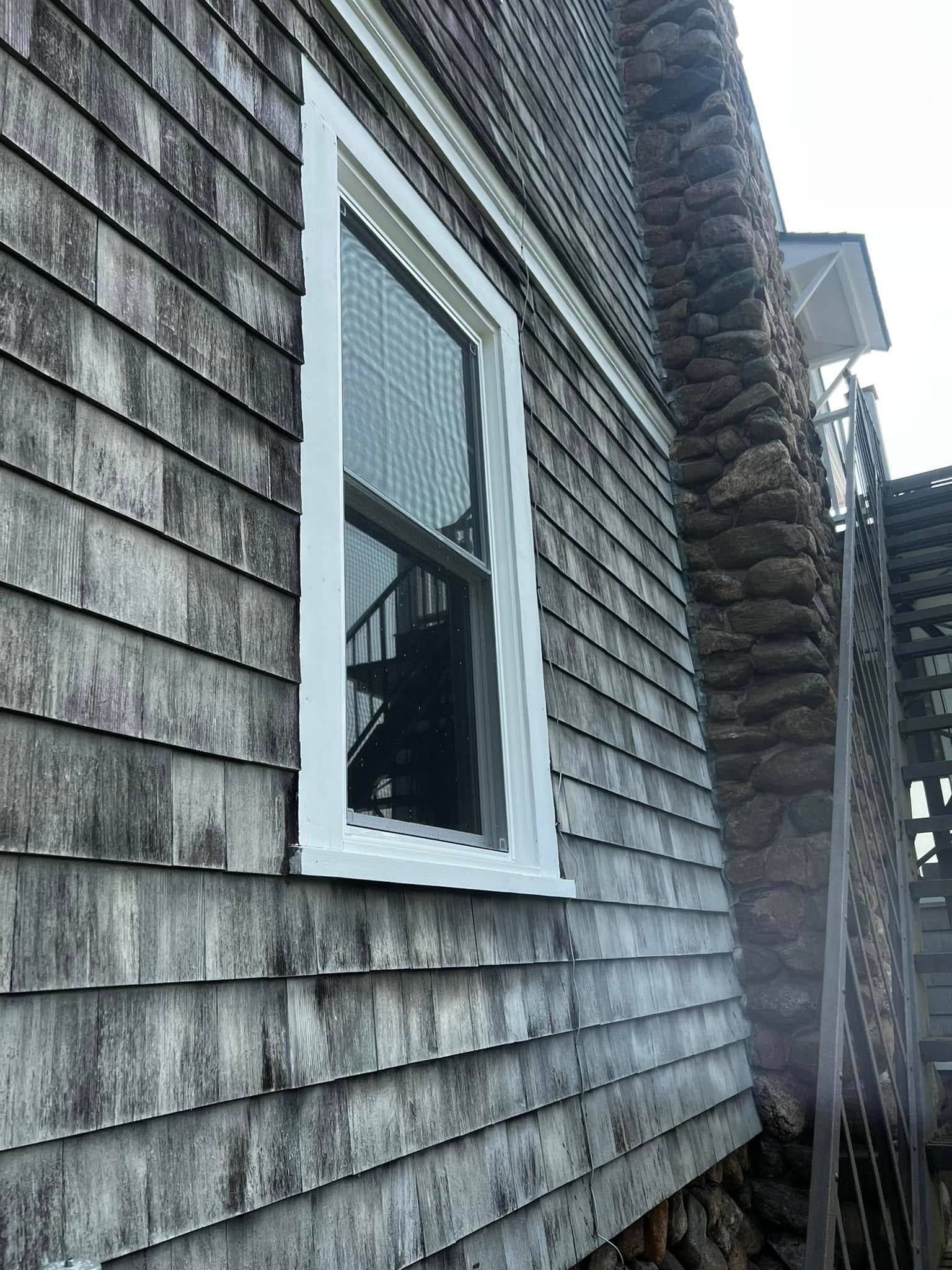 Weathered gray shingle house siding with a white-framed window and deck railing outside