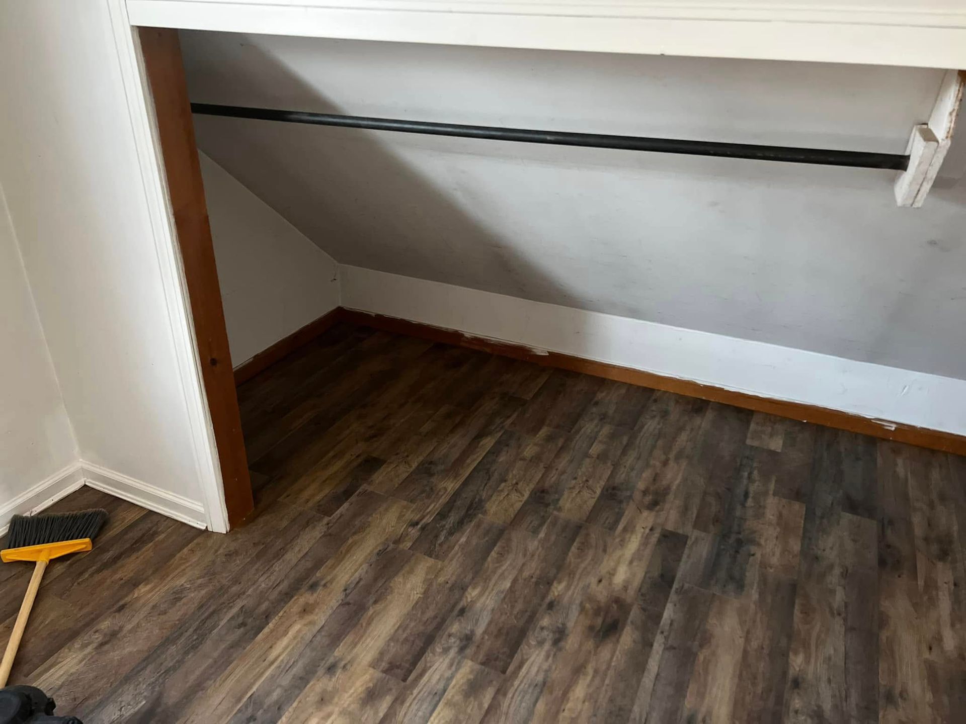 Empty closet with dark wood flooring and a white shelf against slanted walls
