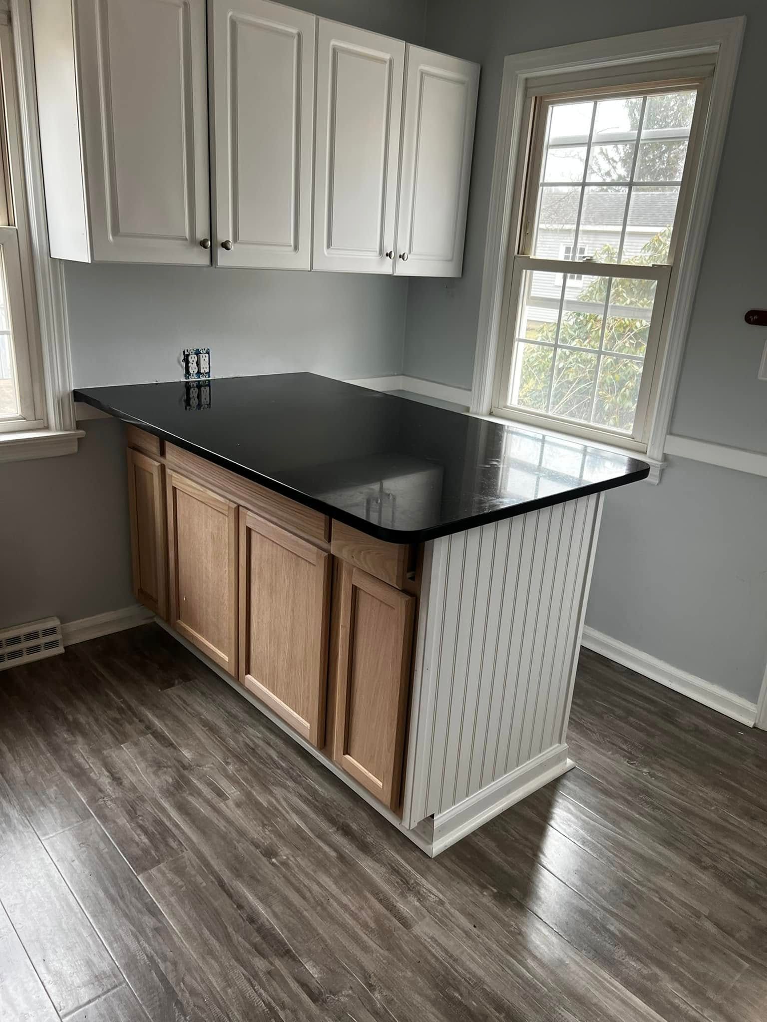 Small kitchen area with white cabinets, black countertop, and a window beside the sink.