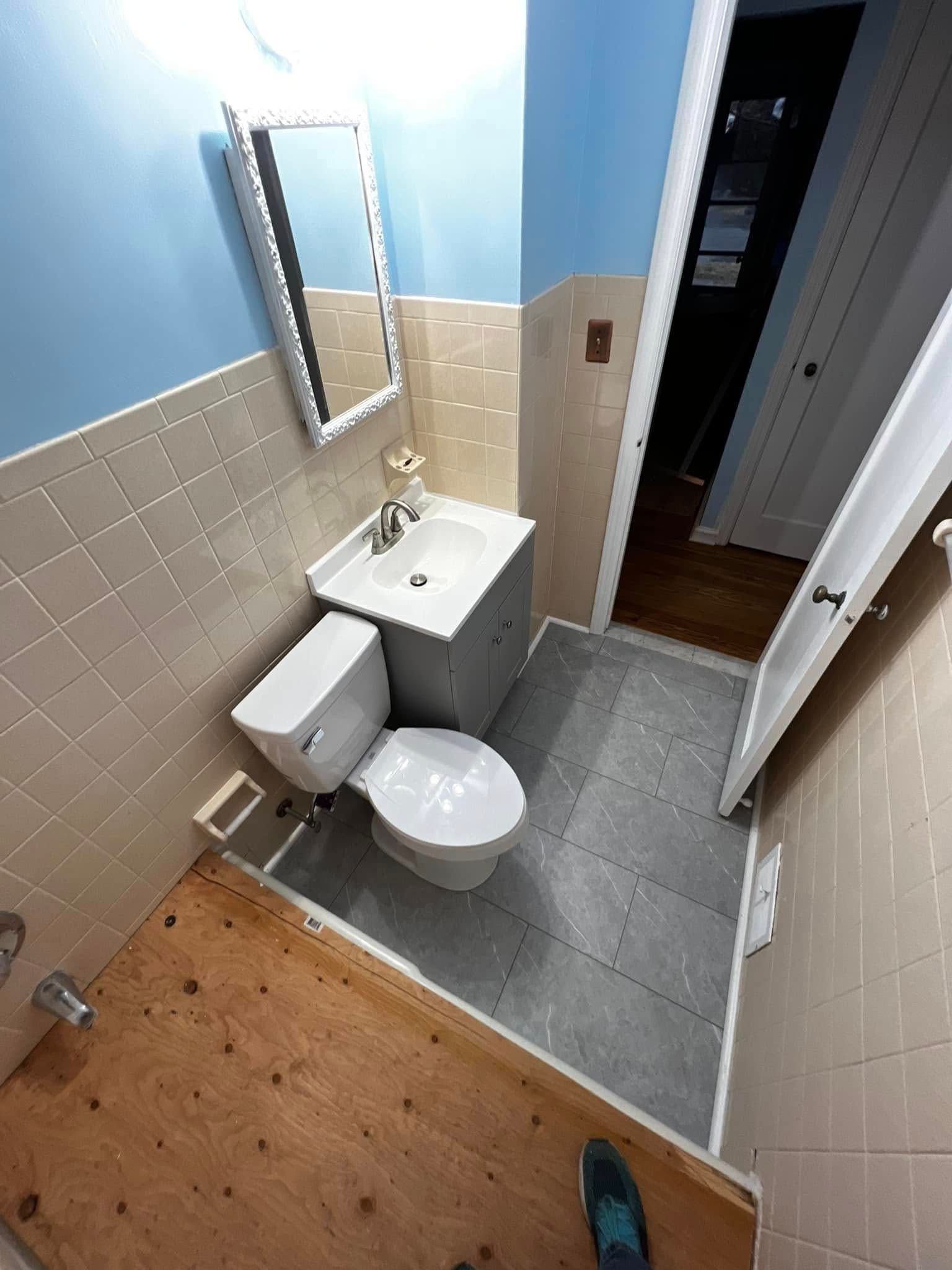 Small bathroom with toilet, sink, mirror, tiled walls, and gray floor, viewed from the doorway