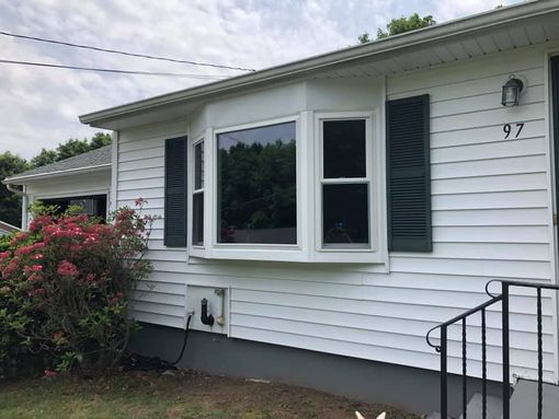 White house front with bay window, dark shutters, pink shrub, and black porch railing numbered 97