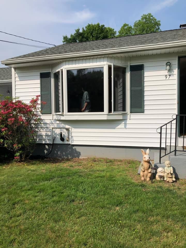 Single-story white house with dark shutters, open window, lawn, and two small dog statues by the front steps