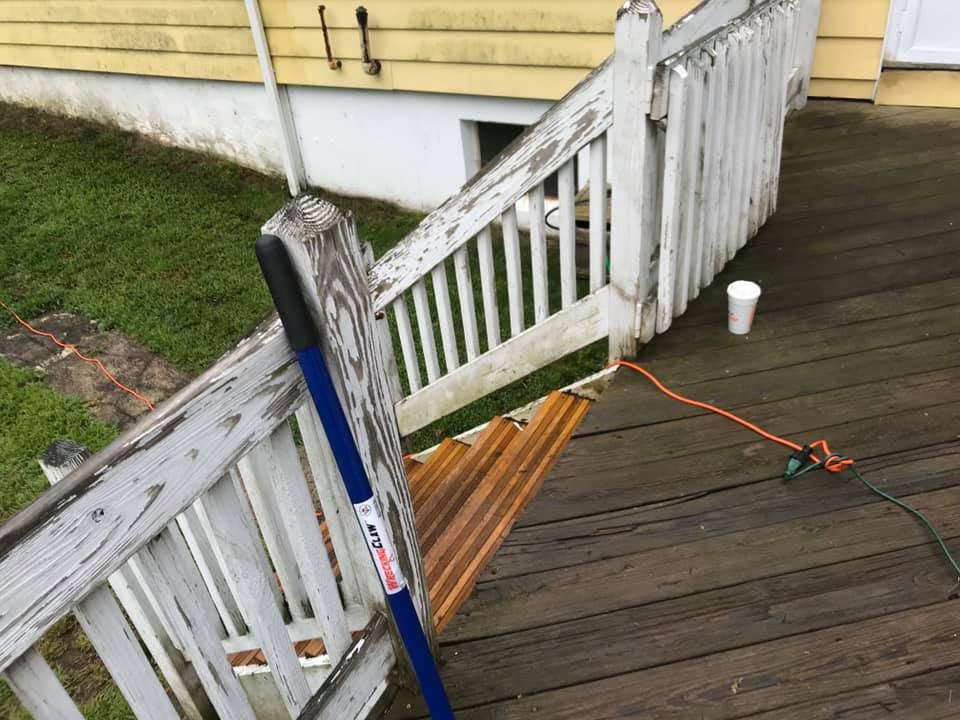 Broken white porch railing beside a wooden deck, with a broom and extension cord on the ground.