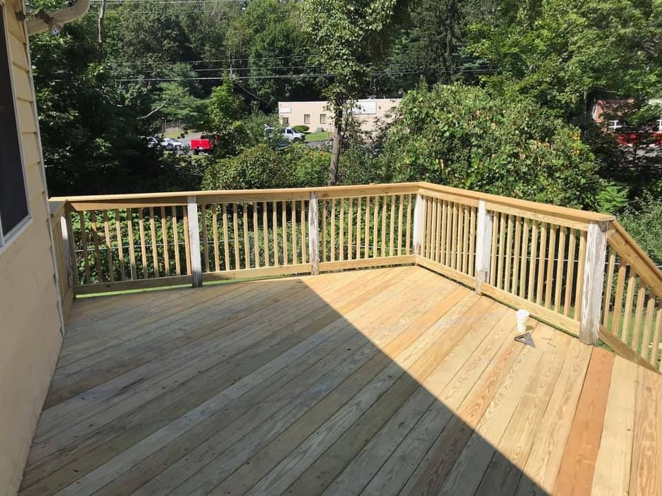 Wooden backyard deck with railings, sunlit floor, and trees and houses beyond.
