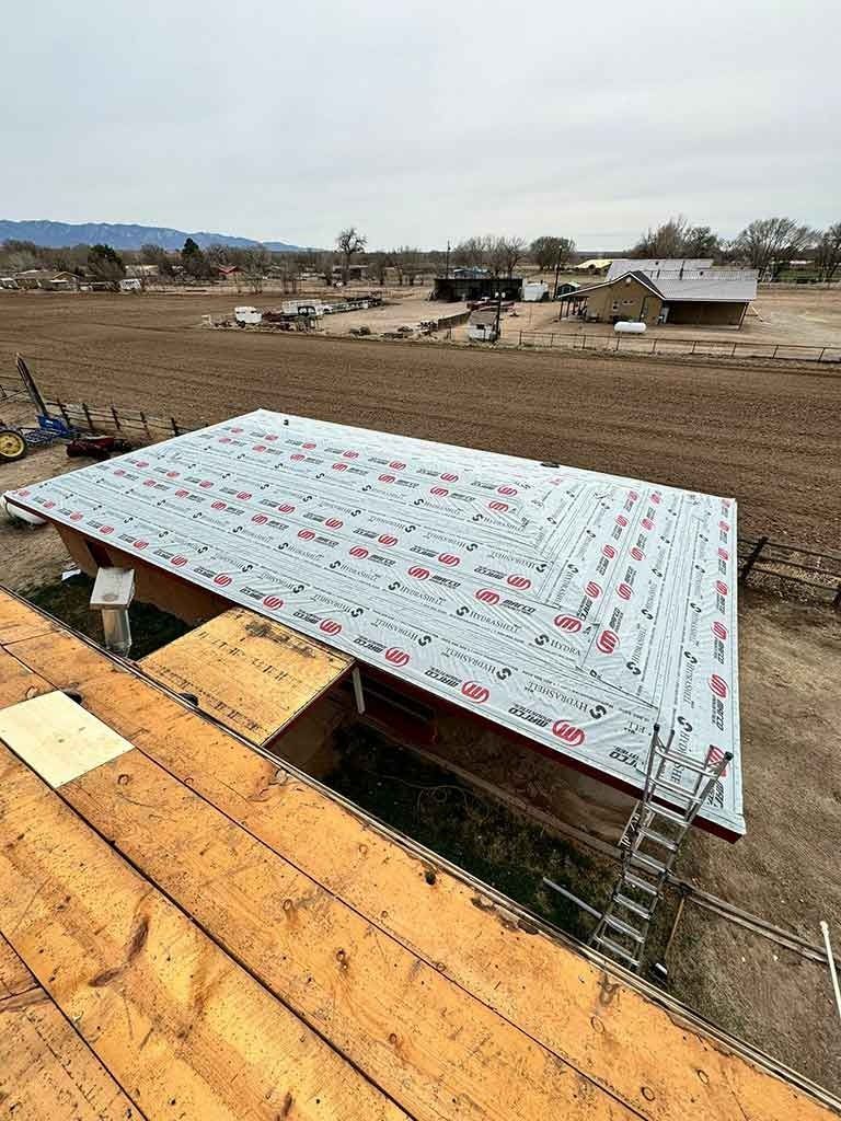New roof deck under construction with white underlayment and exposed plywood in a rural landscape