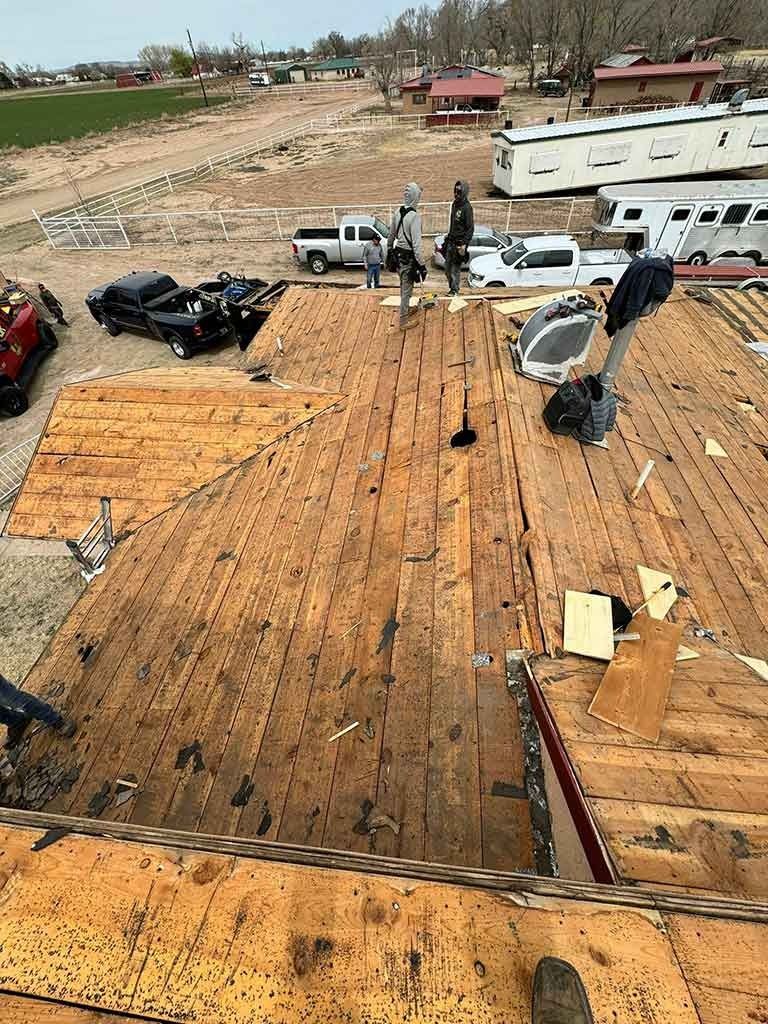 Damaged roof with exposed plywood, parked vehicles, and debris in a lot after severe weather