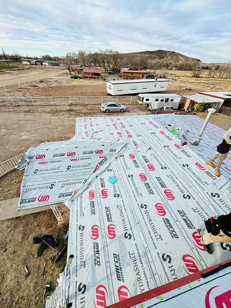Roof under construction in a rural area, with white roofing sheets and nearby trailers.