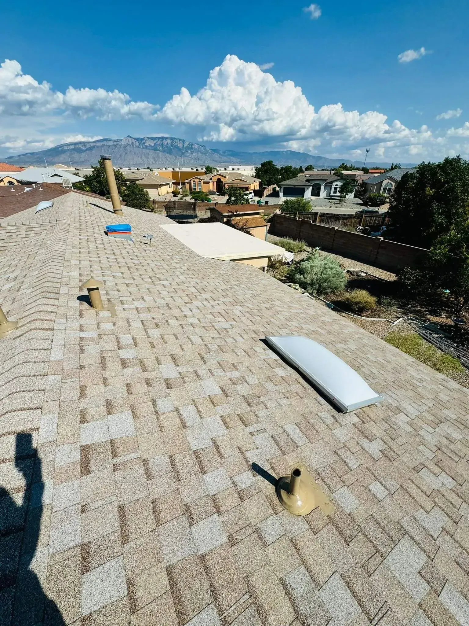 Rooftop with solar panels and skylights overlooking a suburban neighborhood under a blue sky
