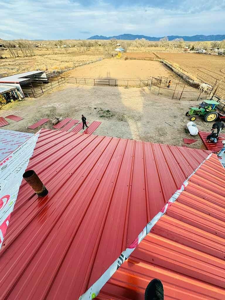 Red metal roof with a person on it, overlooking a sandy construction site under a clear sky.