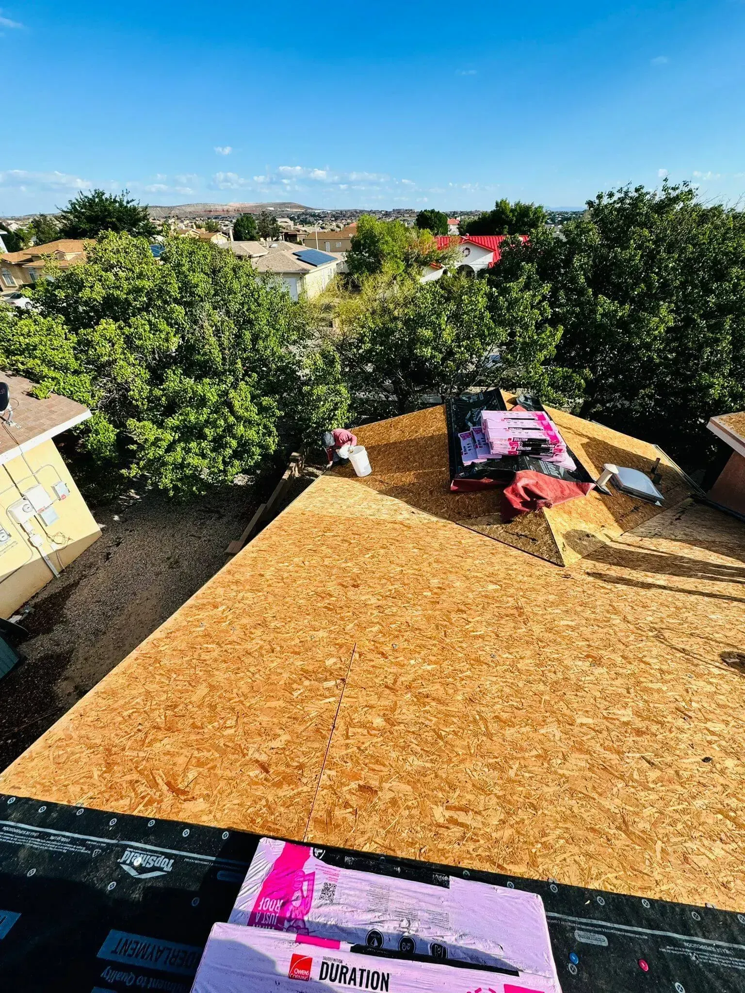 Rooftop patio with tan deck, pink lounge chairs, trees, and a sunny suburban view