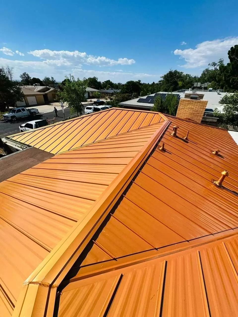 Orange metal rooftop under a blue sky, with vents and trees in the background