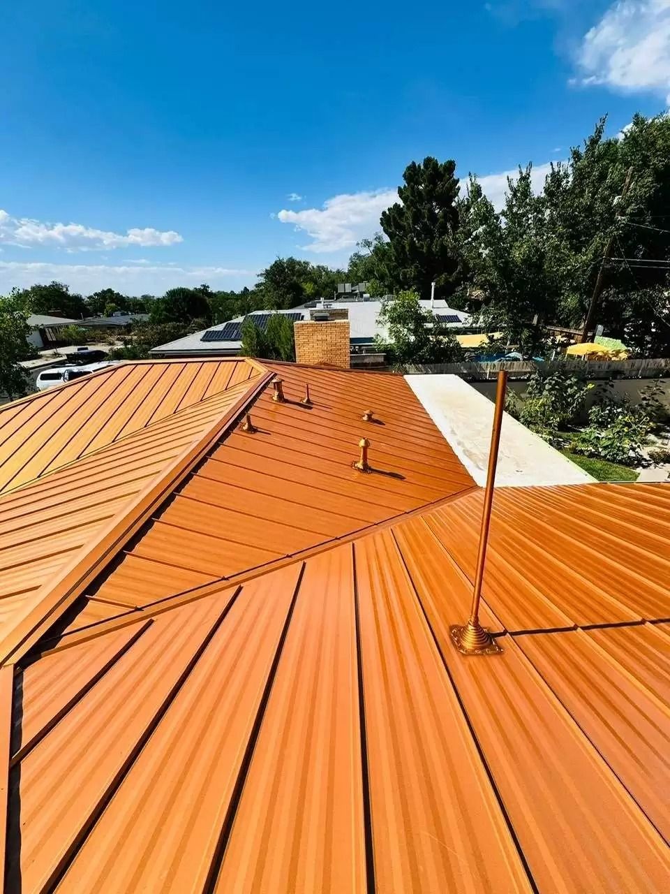 Orange metal roof with skylight and chimney, viewed from above under a blue sky