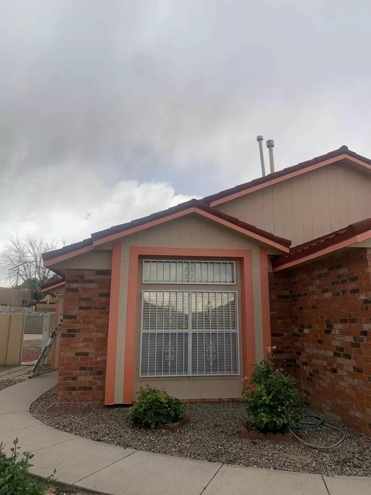 Single-story house exterior with red trim, brick siding, and a window under a cloudy sky