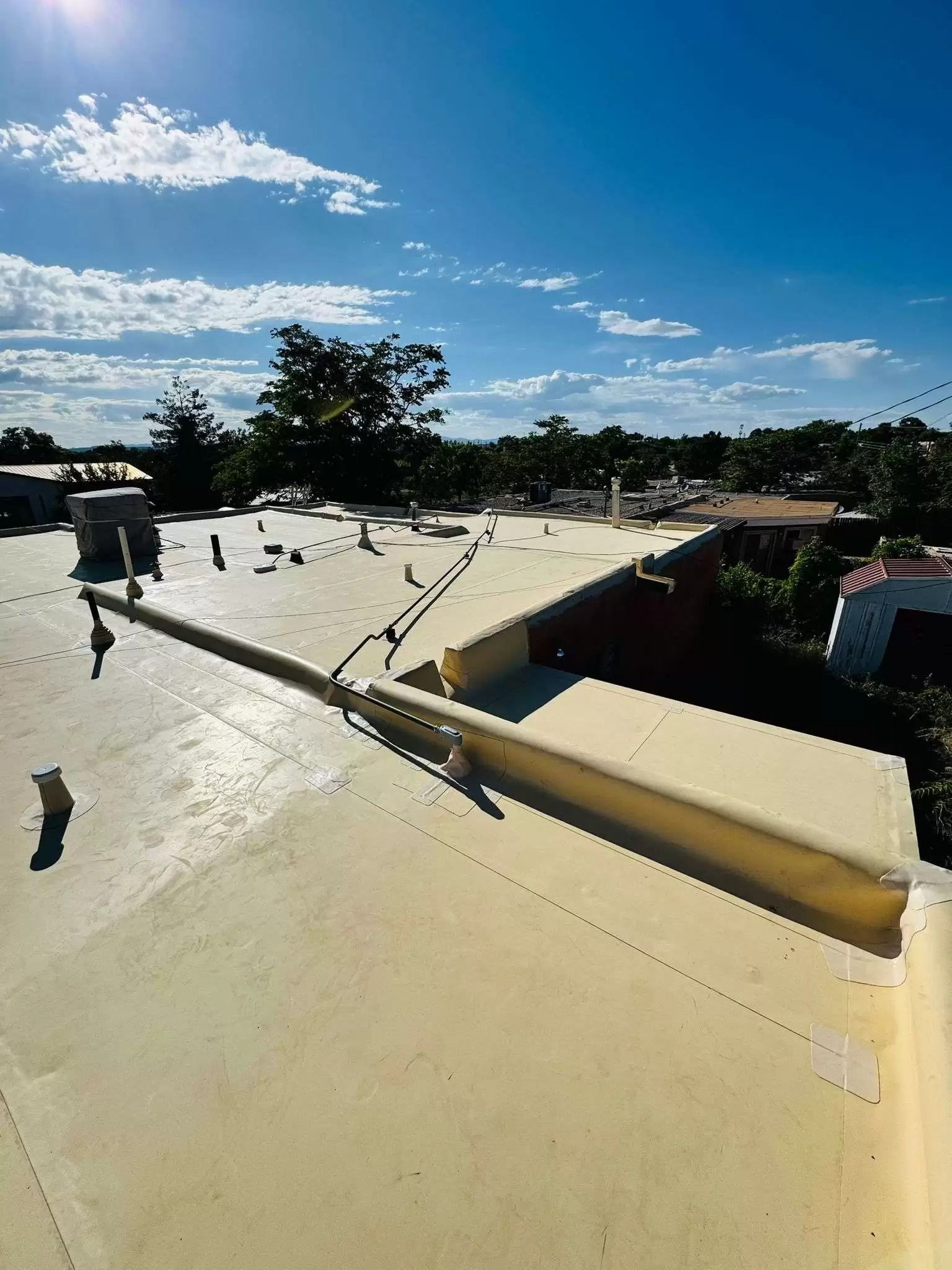 Rooftop with white reflective surface under a blue sky with scattered clouds and trees in the distance