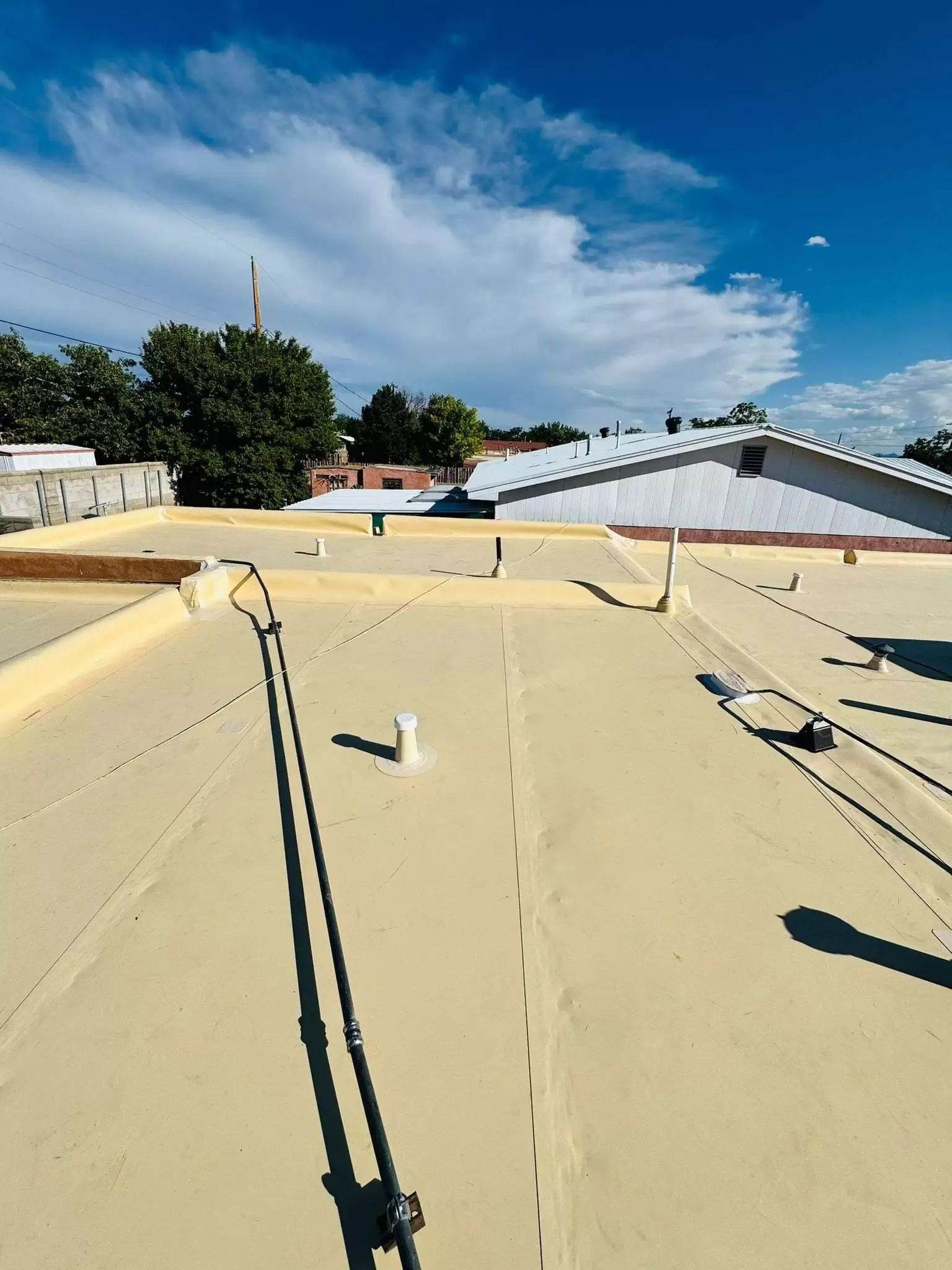 Rooftop with pale yellow surface, metal rails, and distant buildings under a bright blue sky