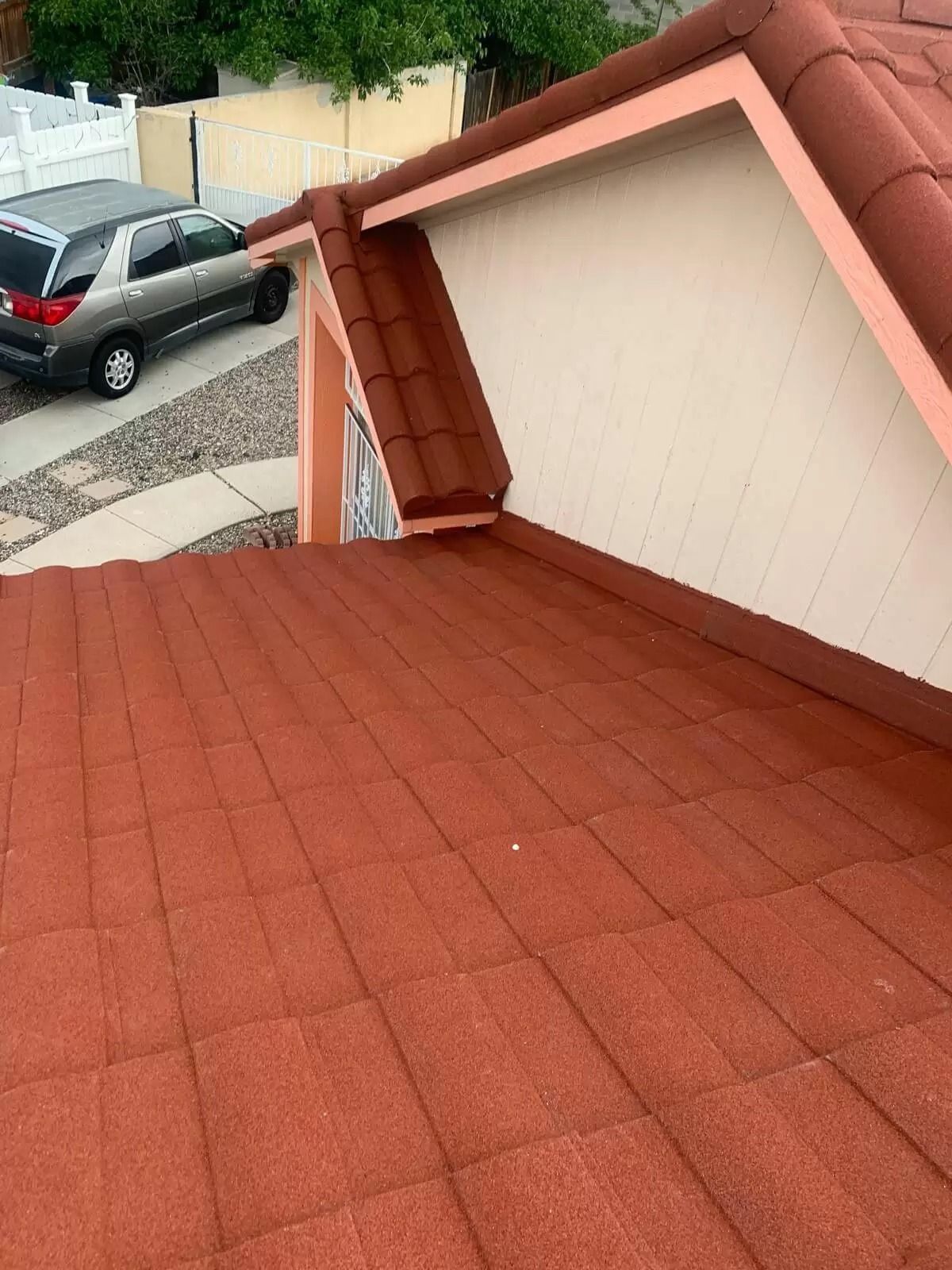 Red roof deck with a damaged corner on a beige house beside a parked car and driveway.